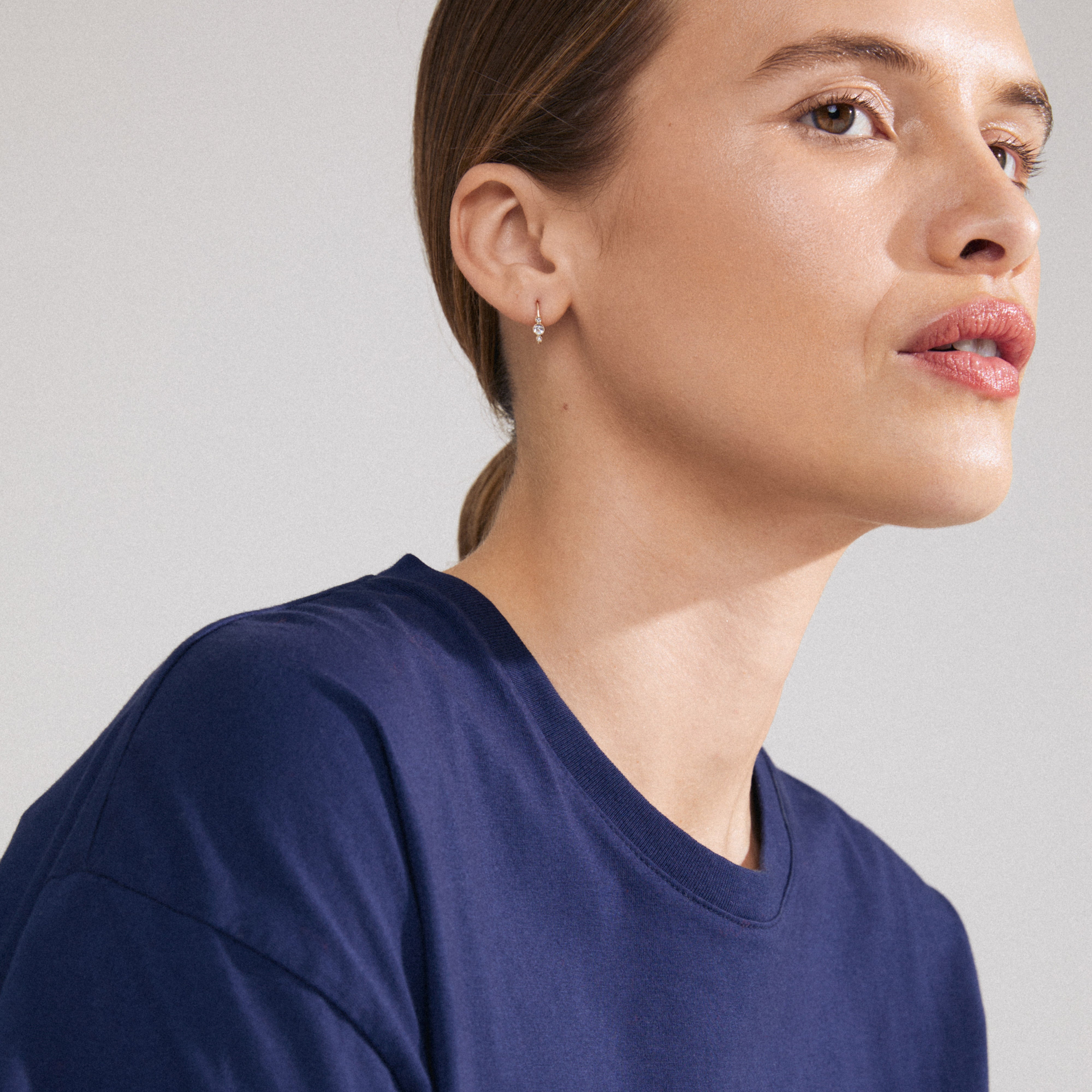 KRISTINE single earring gold-plated with three sparkling Preciosa crystals worn by a woman in a blue shirt, highlighting its elegant design and craftsmanship.