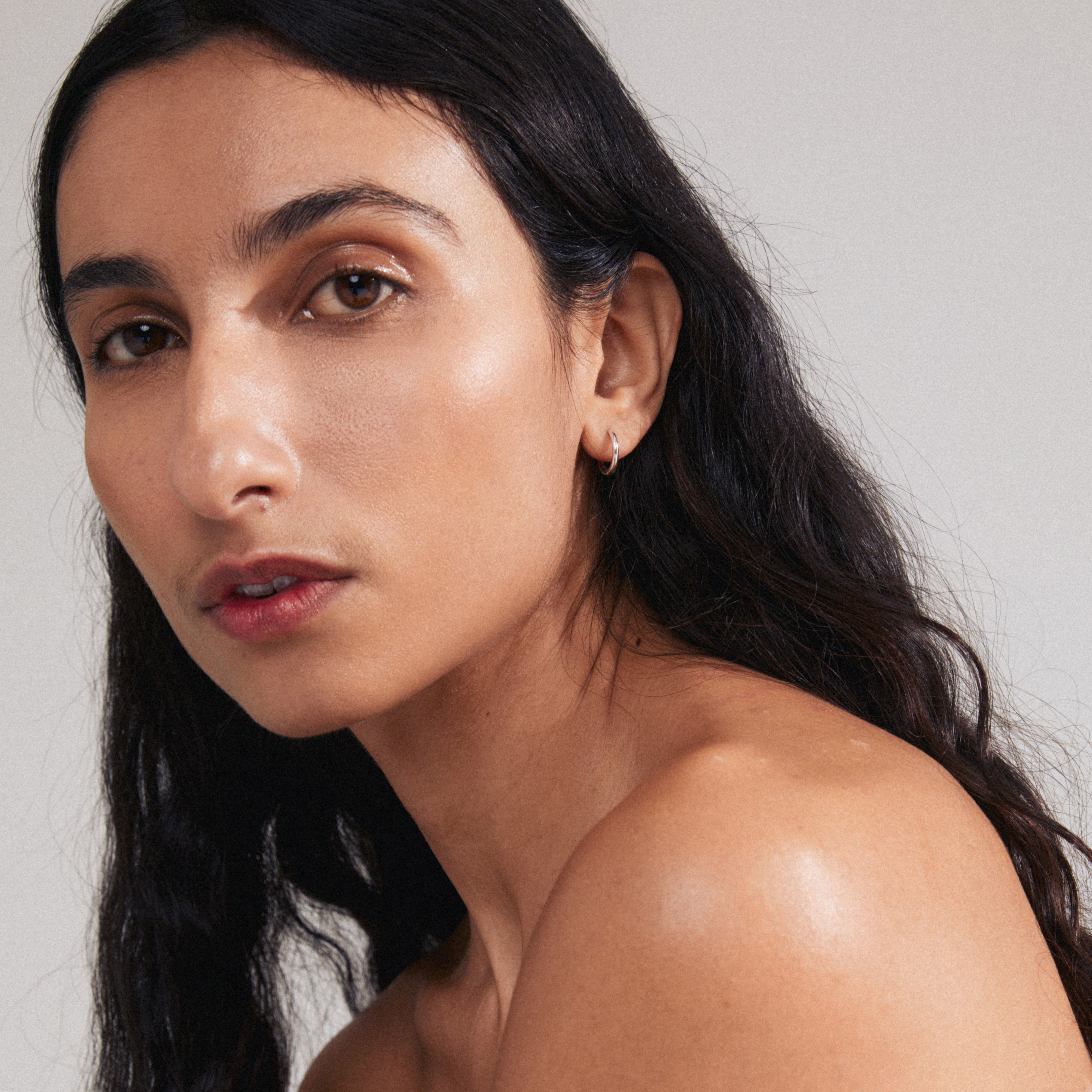 Close-up of a woman wearing the LAVRA single earring, a silver-plated hoop with a shiny finish, highlighting its timeless design and easy click clasp.
