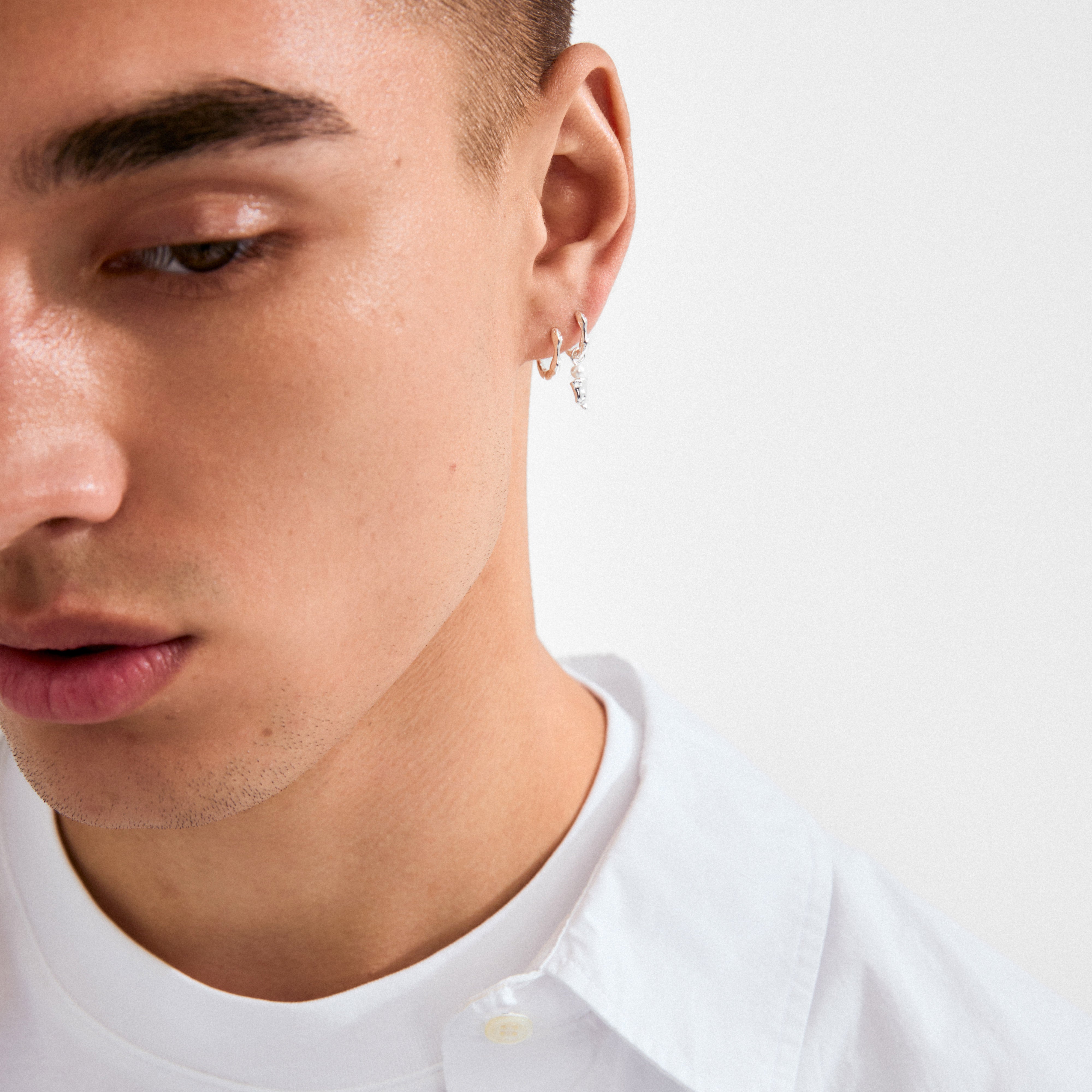 KYRA single earring silver-plated on a young man's ear, featuring a small hoop with a tiny dangling charm, showcasing a sleek, handcrafted design.