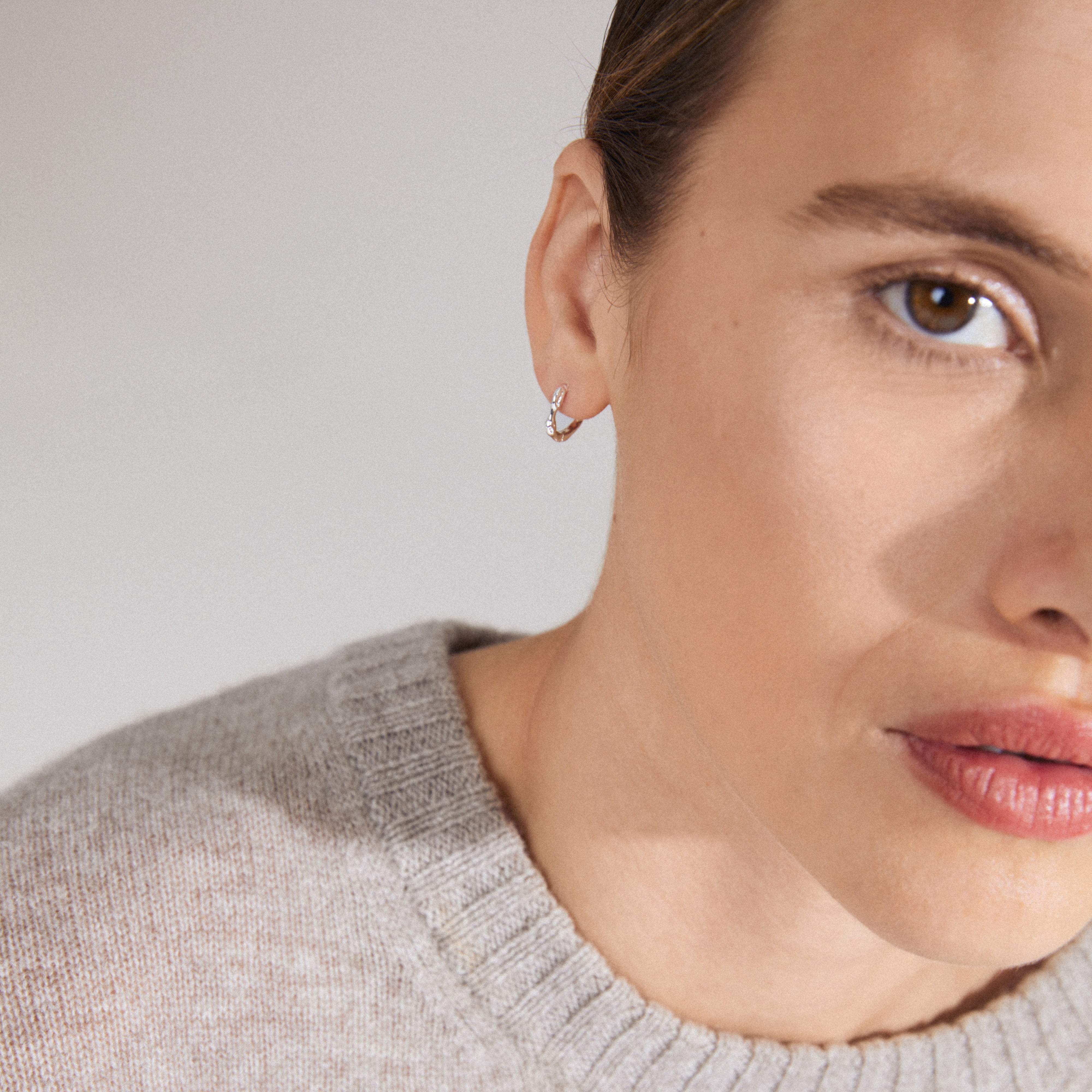 KYRA single earring silver-plated, showcasing its organic shape and shiny finish on a woman's ear, highlighting its timeless, handcrafted design.