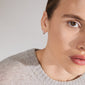 KYRA single earring silver-plated, showcasing its organic shape and shiny finish on a woman's ear, highlighting its timeless, handcrafted design.