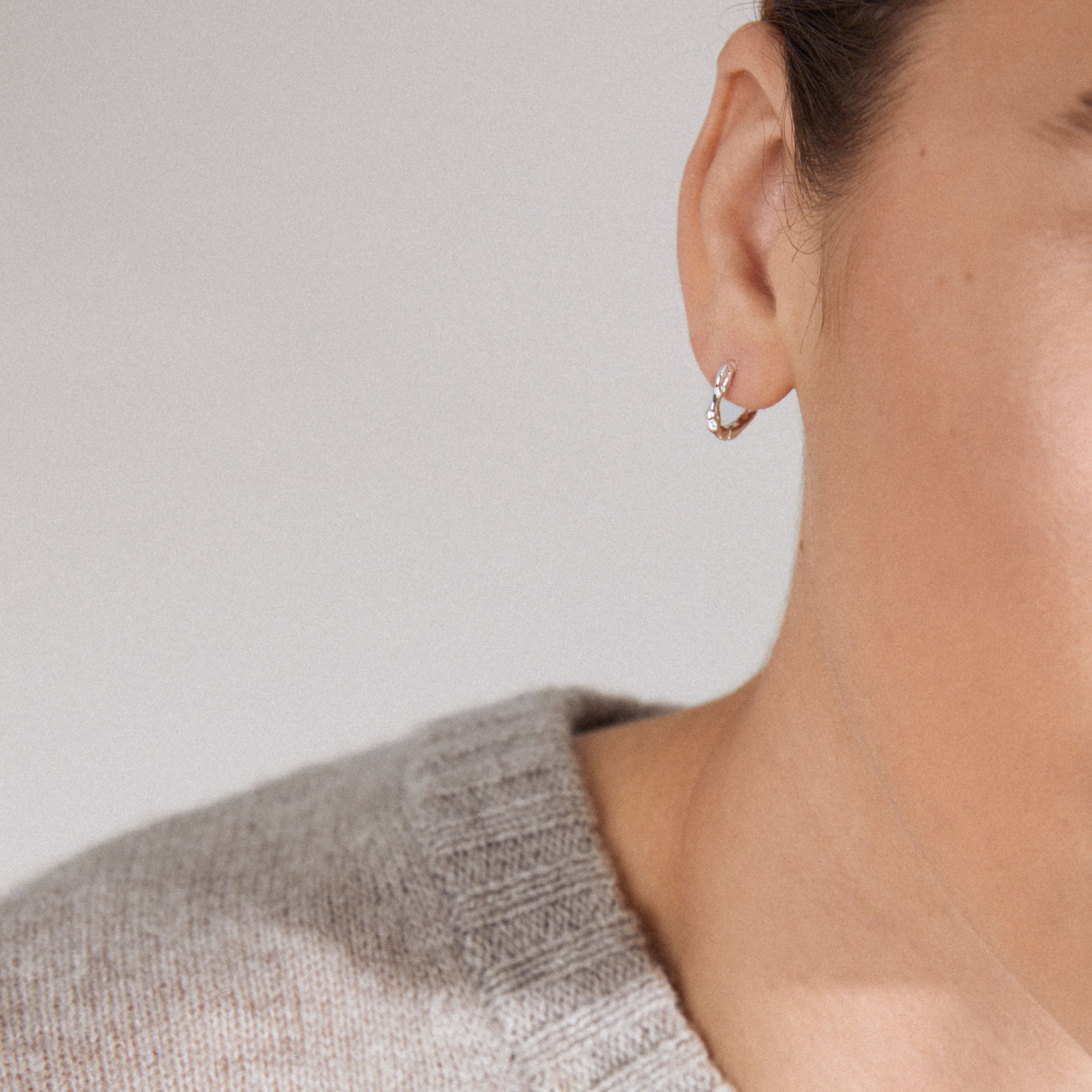 KYRA single earring silver-plated, featuring a twisted design with tiny stones, worn with a light-gray sweater against an off-white background.