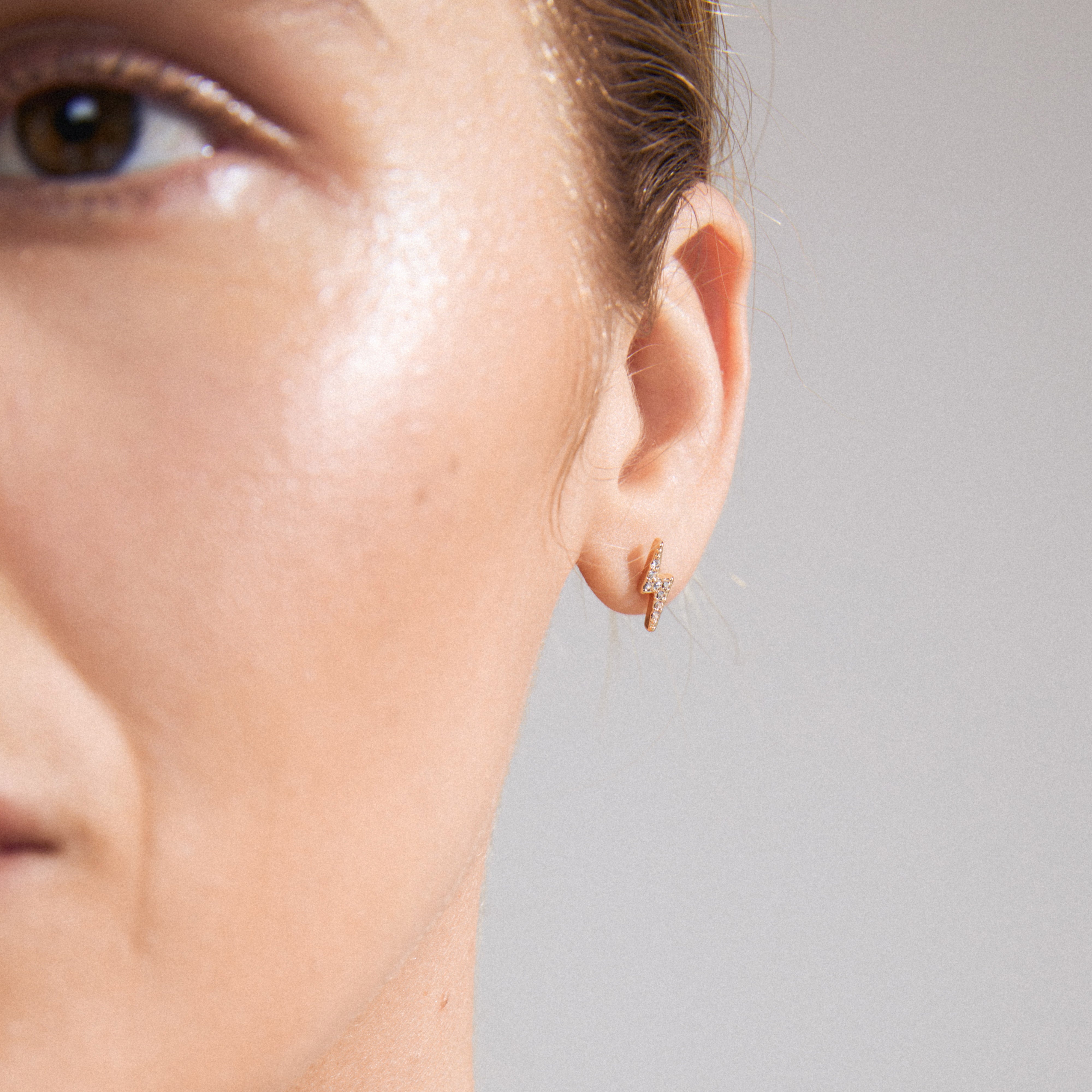 ADONIS single earring gold-plated, featuring a lightning bolt design with Preciosa crystals, shown on a woman's ear, highlighting its elegant and trendy style.