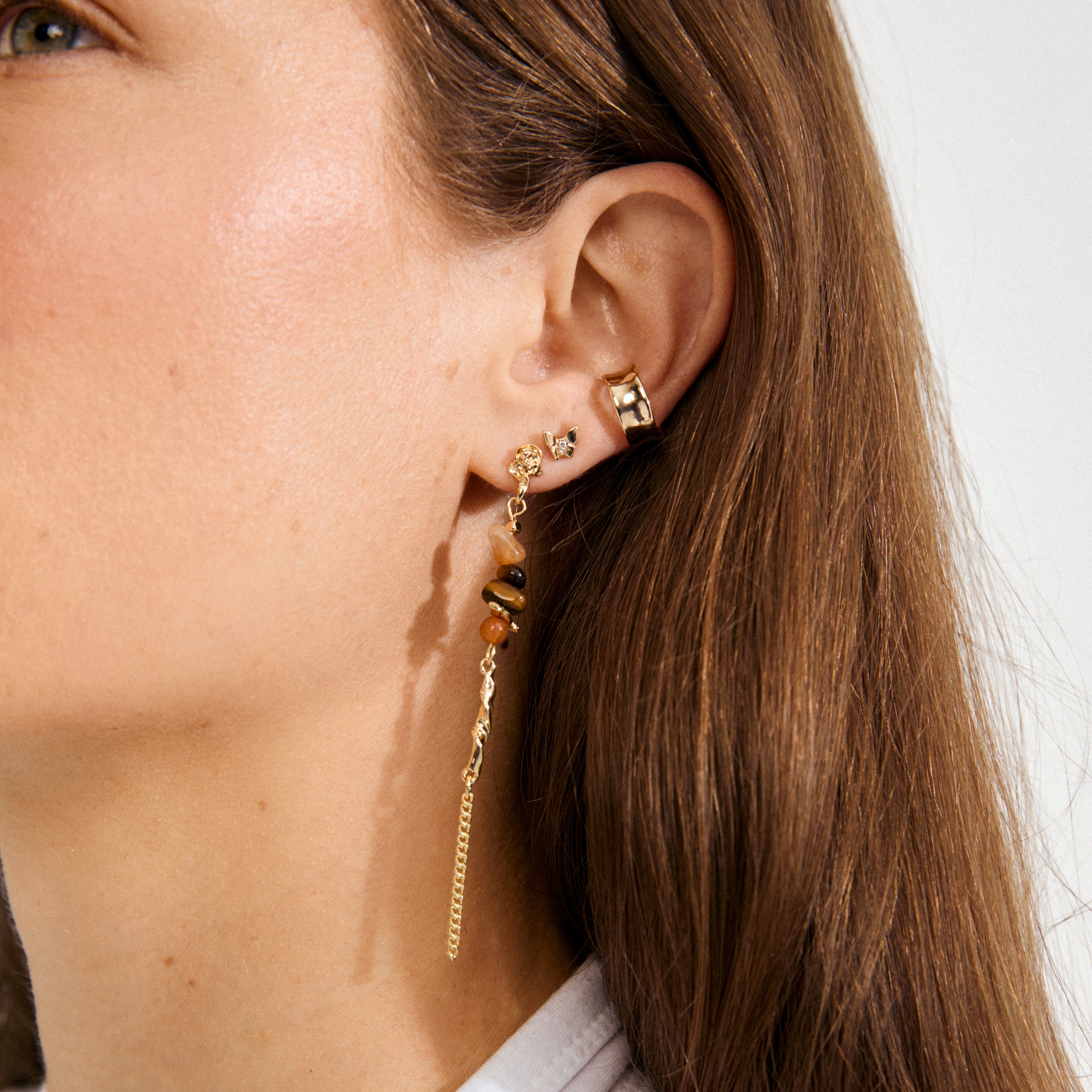 Close-up of an ear adorned with a gold-plated SKYLER ear cuff by Pilgrim, alongside other earrings, showcasing a stylish layered look.