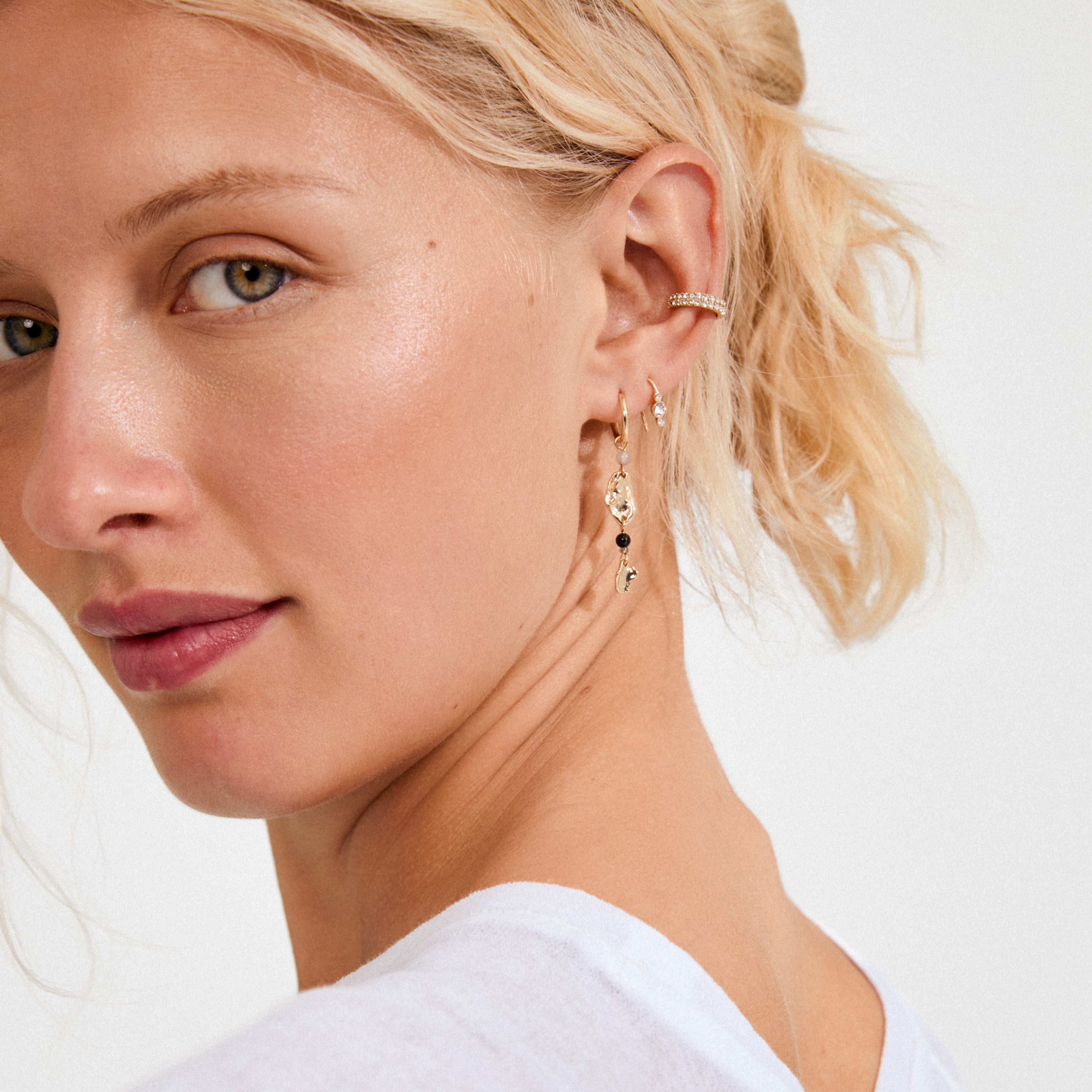 KEEGAN ear cuff gold-plated with sparkling Preciosa crystals, elegantly accenting a young woman's ear alongside gold hoops and a drop earring, exuding effortless glam.