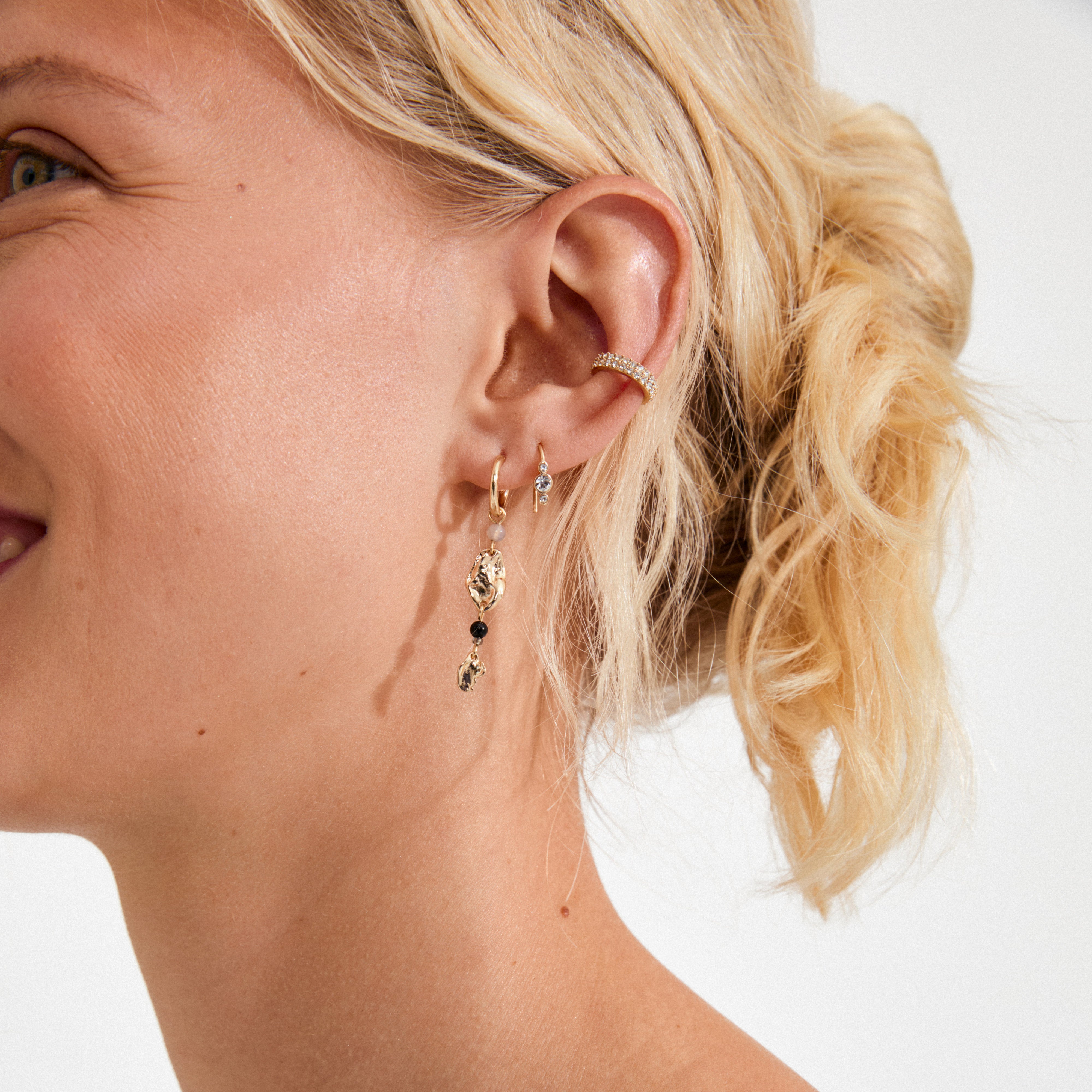 Close-up of a person's ear showcasing the KEEGAN gold-plated ear cuff adorned with Preciosa crystals, adding elegant sparkle to a curated ear look.
