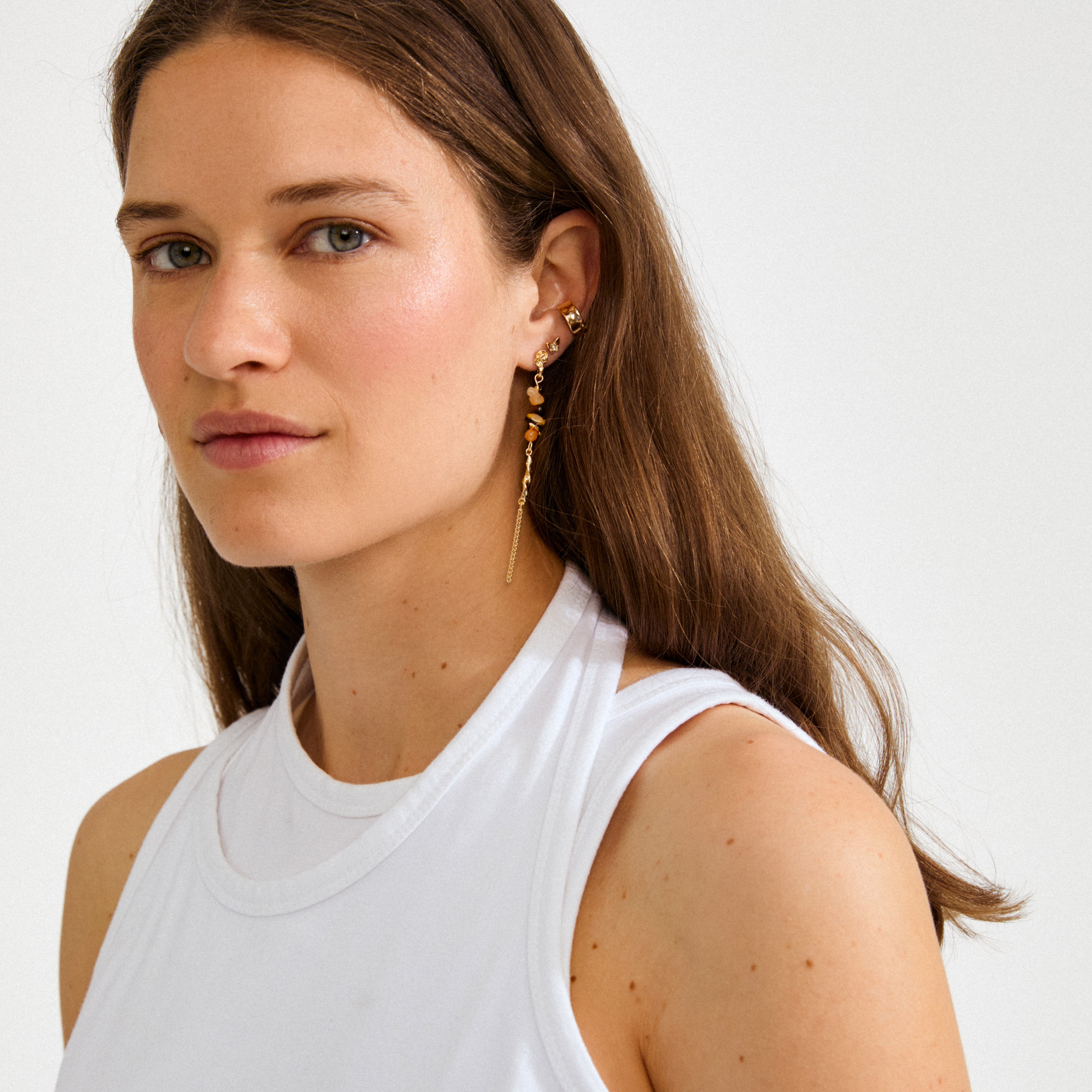 Young woman wearing the SUTTON single earring gold-plated, showcasing boho elegance with gold chain links and amber-colored stones. Ideal for a unique, boho-chic look.