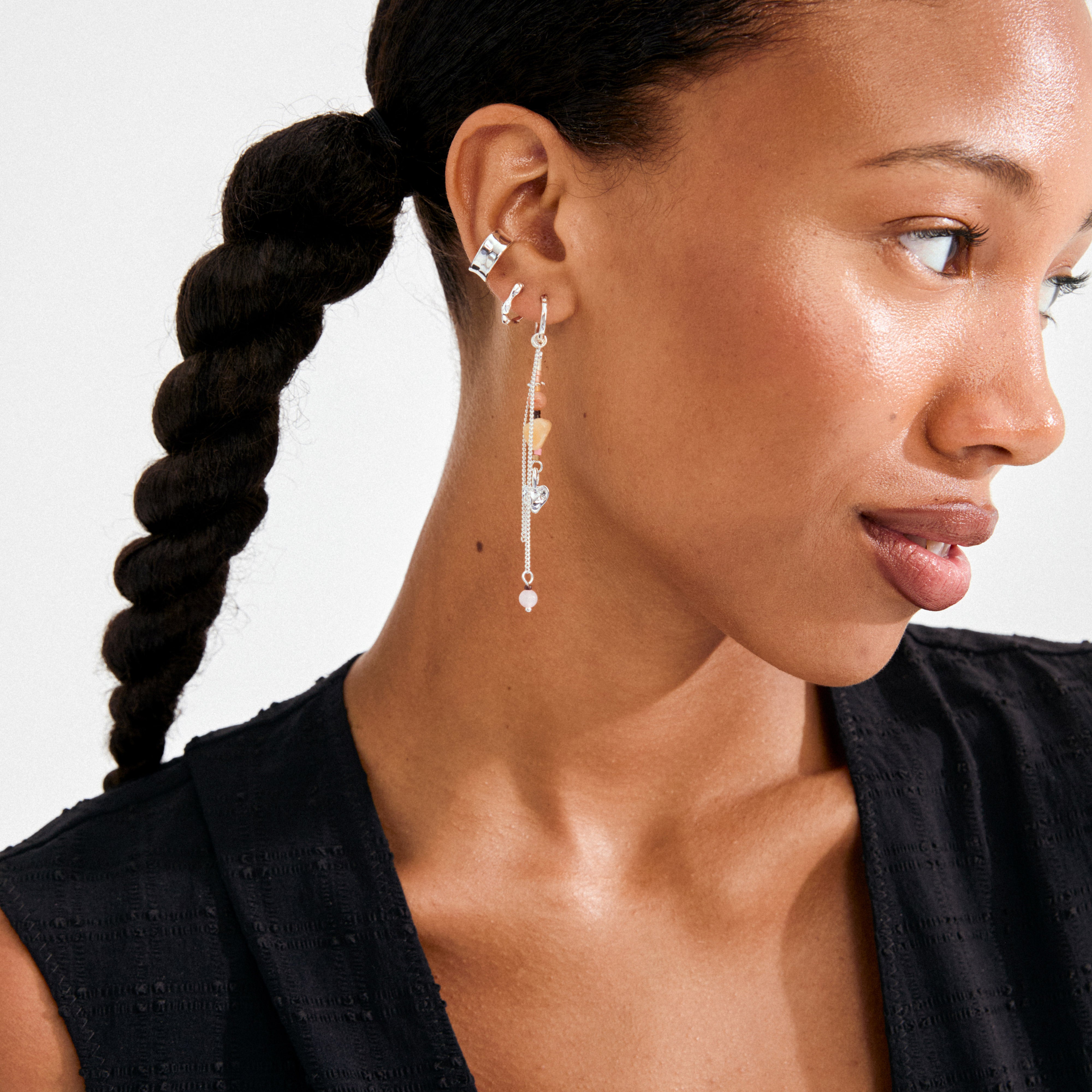 Woman wearing a SKYLER ear cuff, a silver-plated piece from Pilgrim, styled with a hoop and chain earring, highlighting its trendy, recycled design.