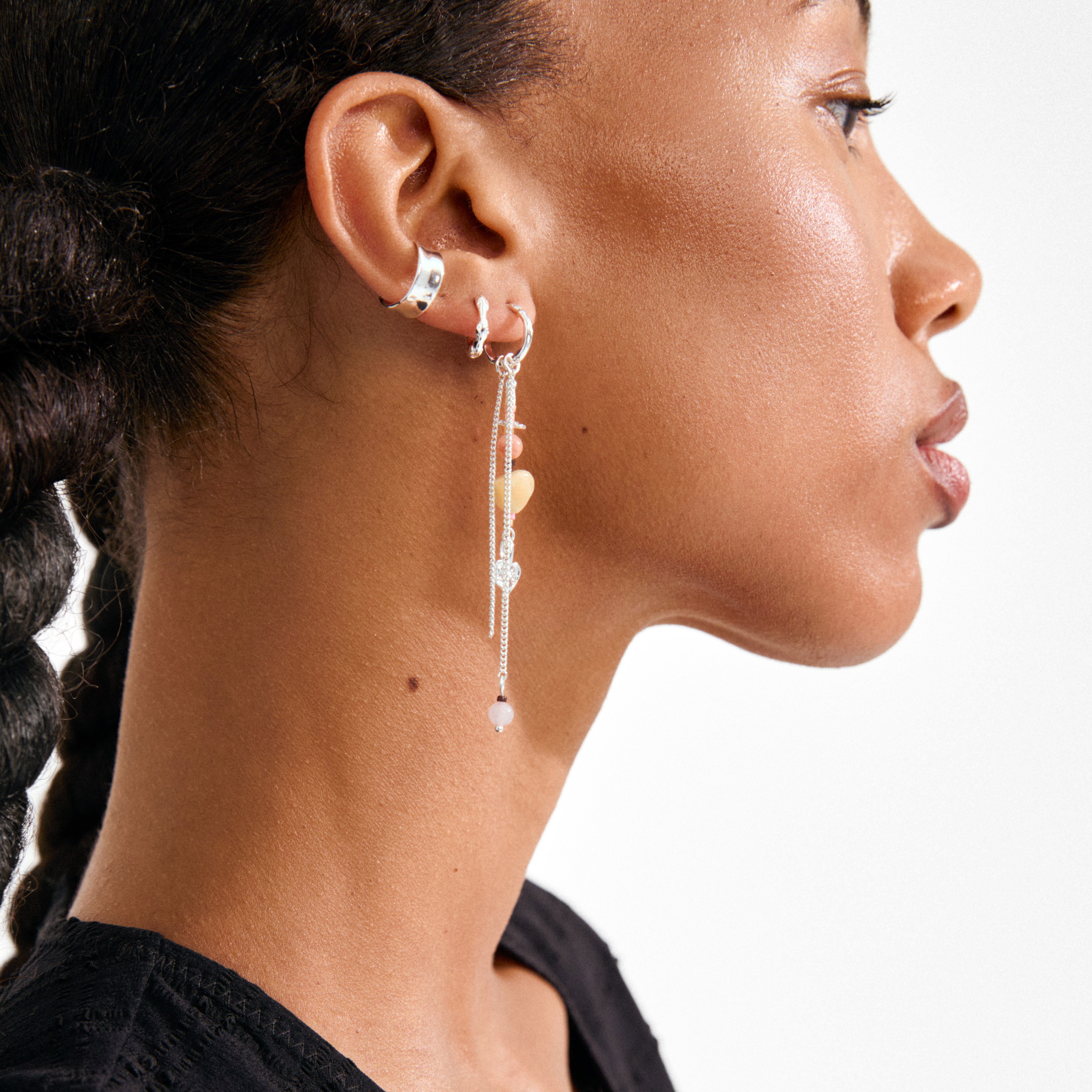 SKYLER ear cuff silver-plated on a person's ear, combining with other silver-tone earrings and showcasing delicate chains and pastel beads. A recycled, trendy Pilgrim piece.