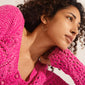 Young woman wears Pilgrim's ROMINA gold-plated hoop earring, featuring metallic beads, paired with a bright pink crocheted sweater, embodying a stylish, feminine summer look.