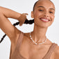 Young woman wearing Pilgrim's RAMONA freshwater pearl necklace, featuring sculptural pearls and rose quartz, exuding natural beauty and soft femininity. She smiles, showcasing the necklace's playful design.