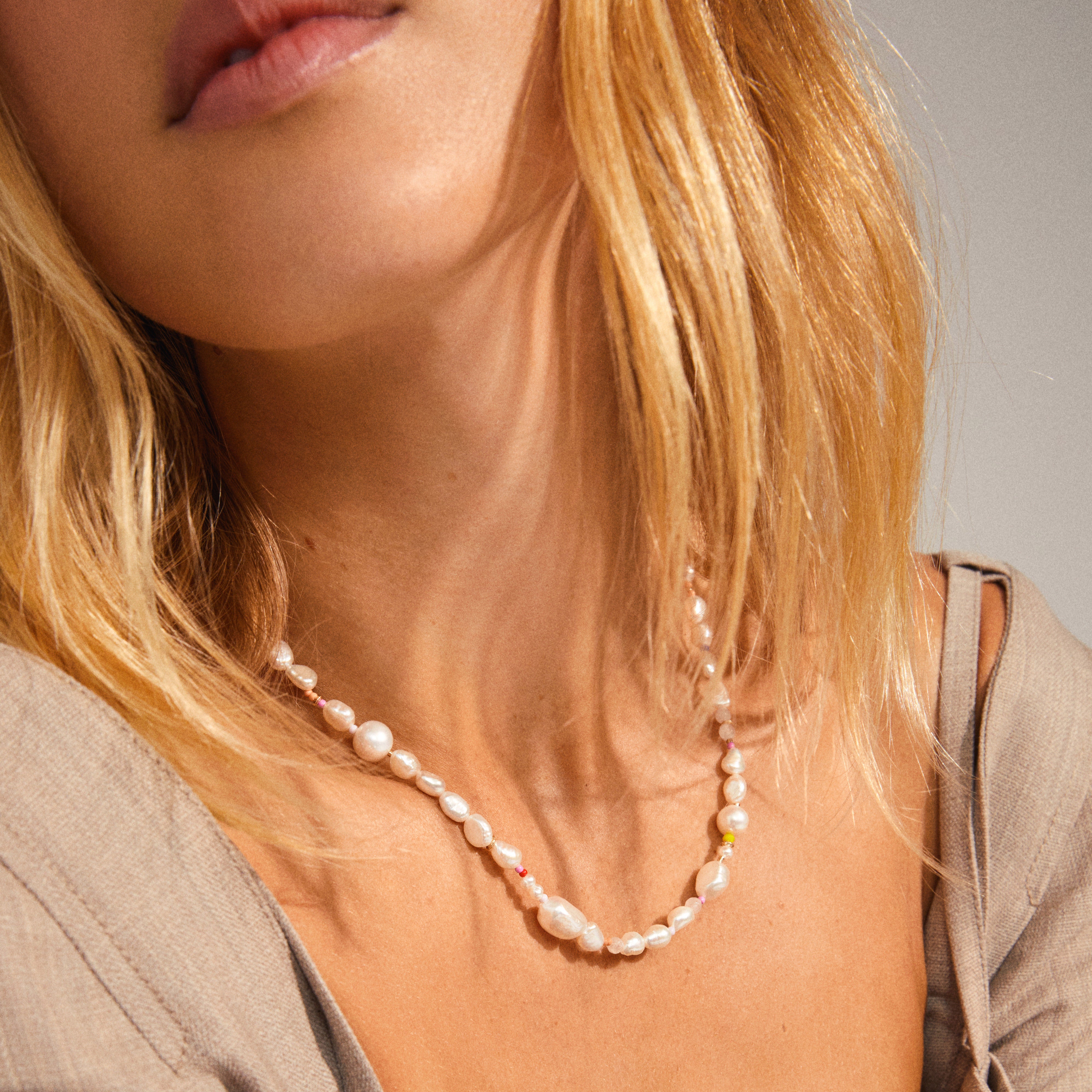 Woman wearing the RAMONA freshwater pearl necklace, gold-plated, with organic pearls and rose quartz stones, showcasing elegance and playful multi-colored details.