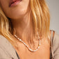 Woman wearing the RAMONA freshwater pearl necklace, gold-plated, with organic pearls and rose quartz stones, showcasing elegance and playful multi-colored details.
