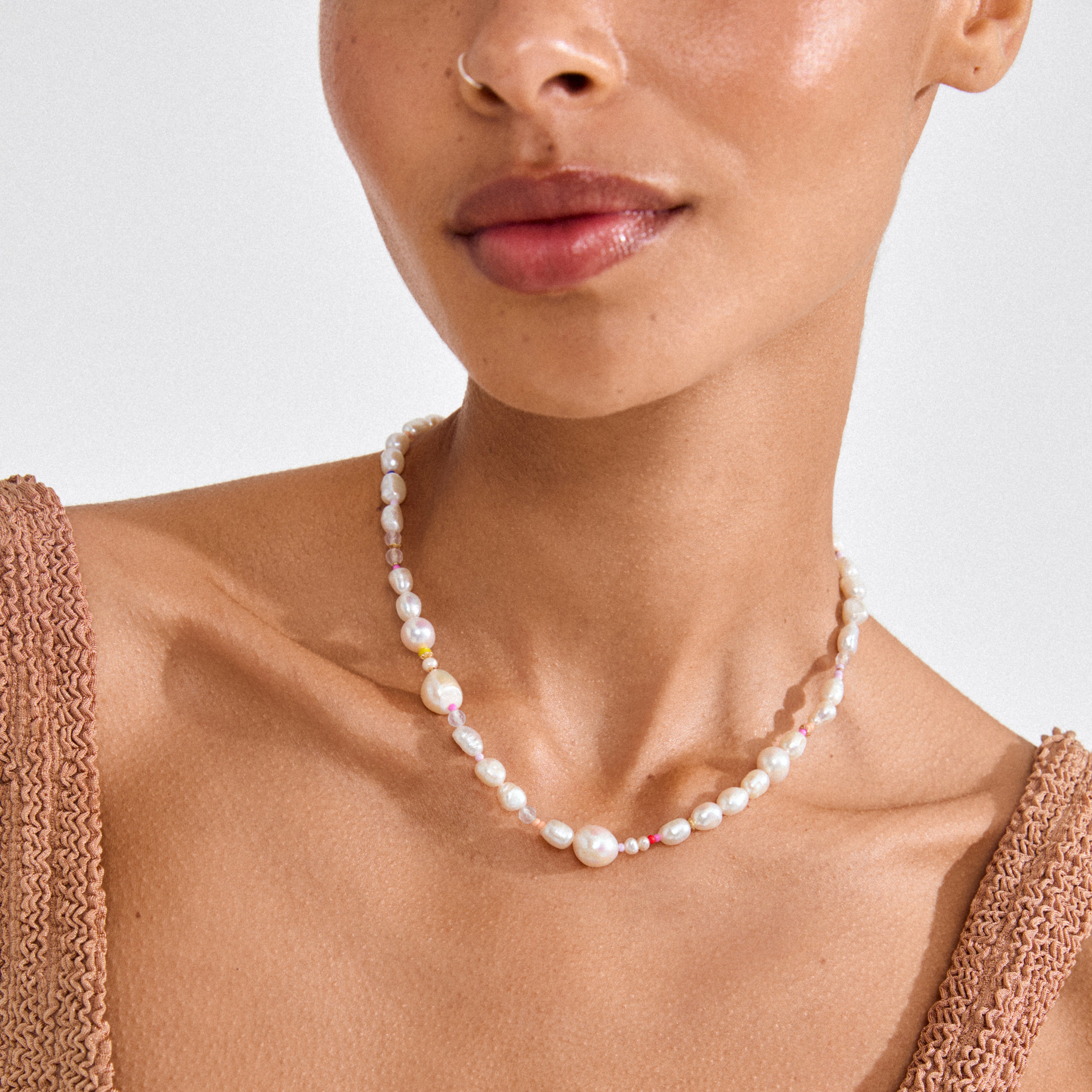 Close-up of a woman wearing Pilgrim's RAMONA freshwater pearl necklace, featuring irregular pearls and colorful beads, highlighting natural beauty and individuality.