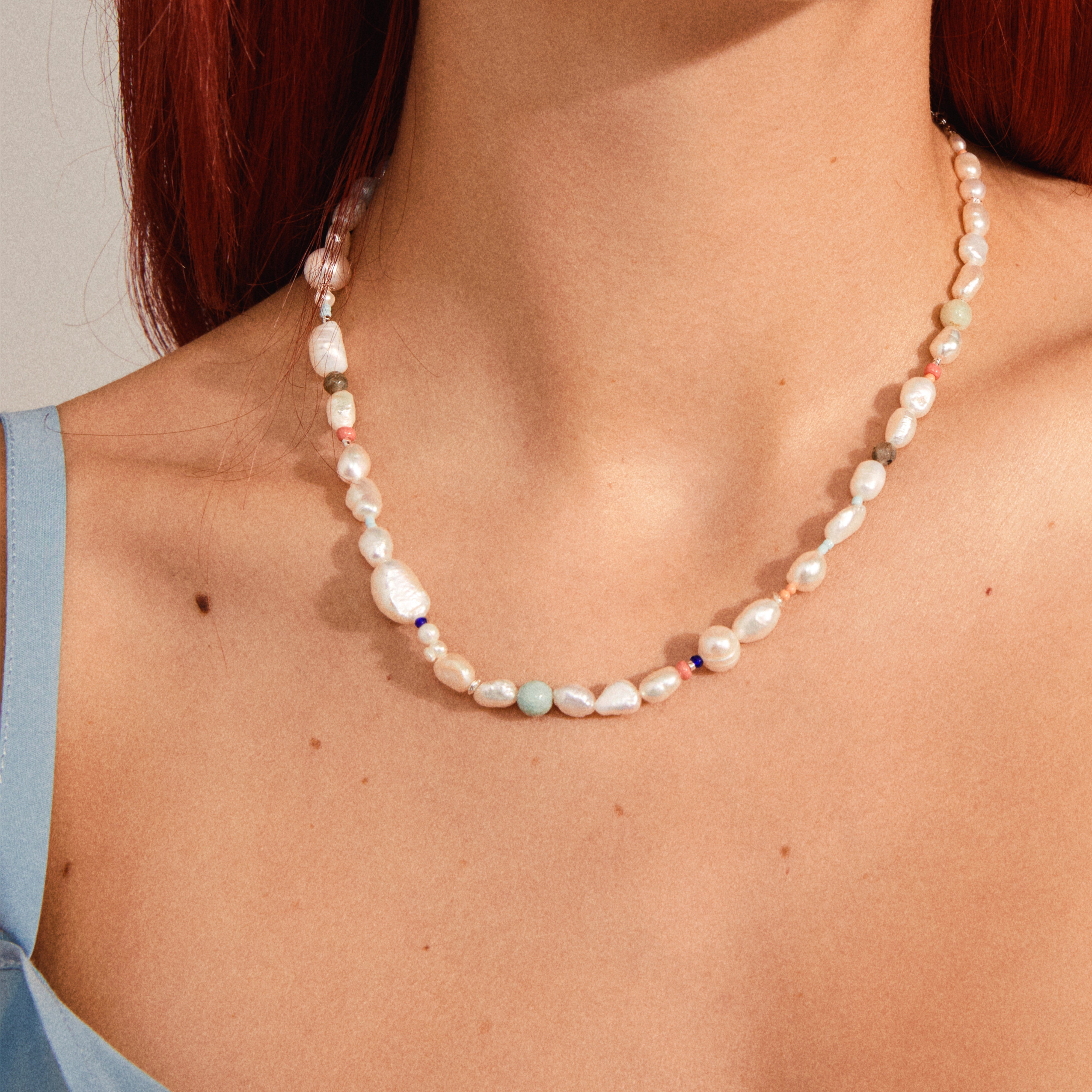 RAMONA freshwater pearl necklace silver-plated features irregular pearls and colored gemstones, elegantly accenting a light blue top on a model's neck and décolletage.