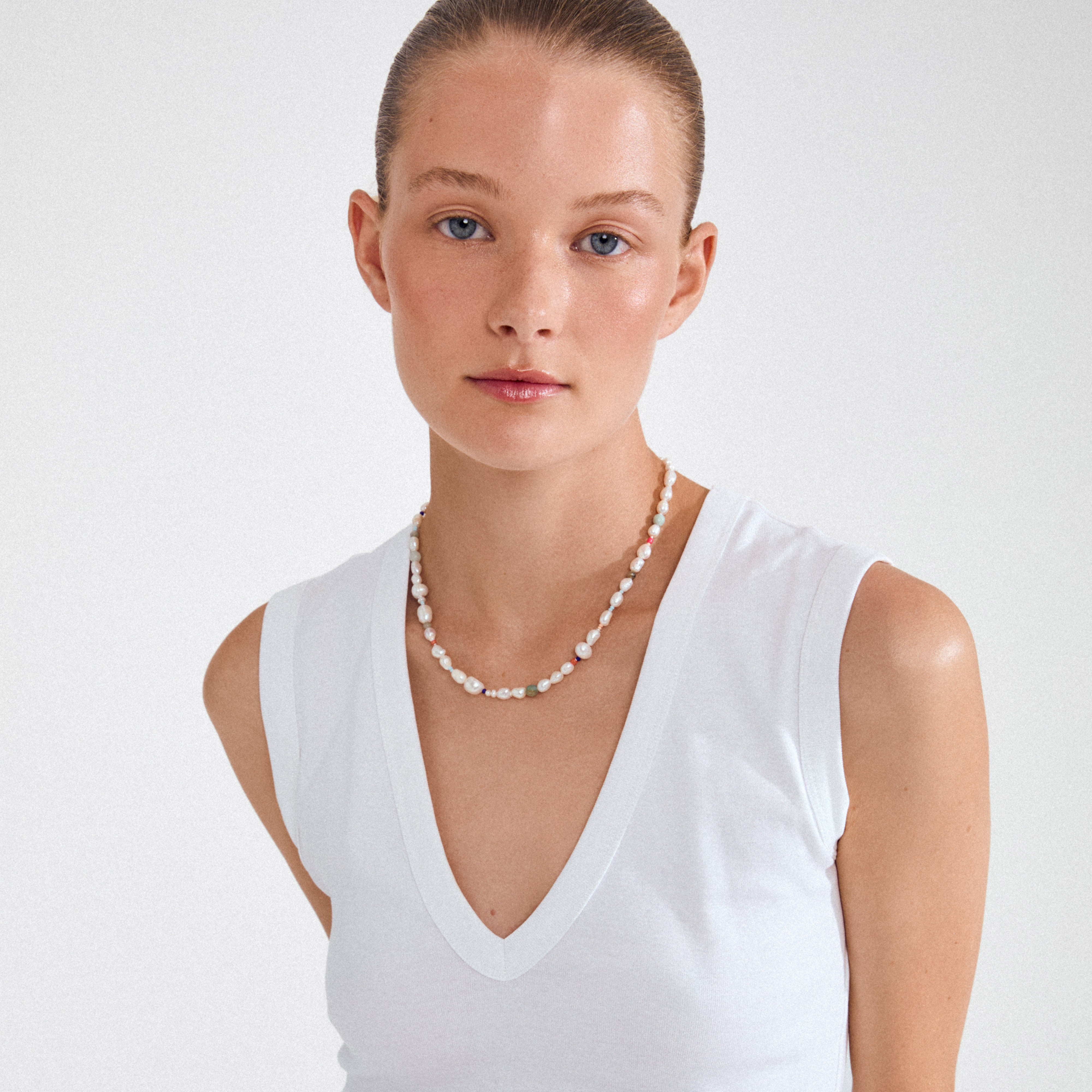 Young woman wearing Pilgrim’s RAMONA freshwater pearl necklace, featuring sculptural pearls and colored beads, styled with a white sleeveless V-neck top.