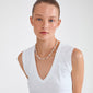 Young woman wearing Pilgrim’s RAMONA freshwater pearl necklace, featuring sculptural pearls and colored beads, styled with a white sleeveless V-neck top.