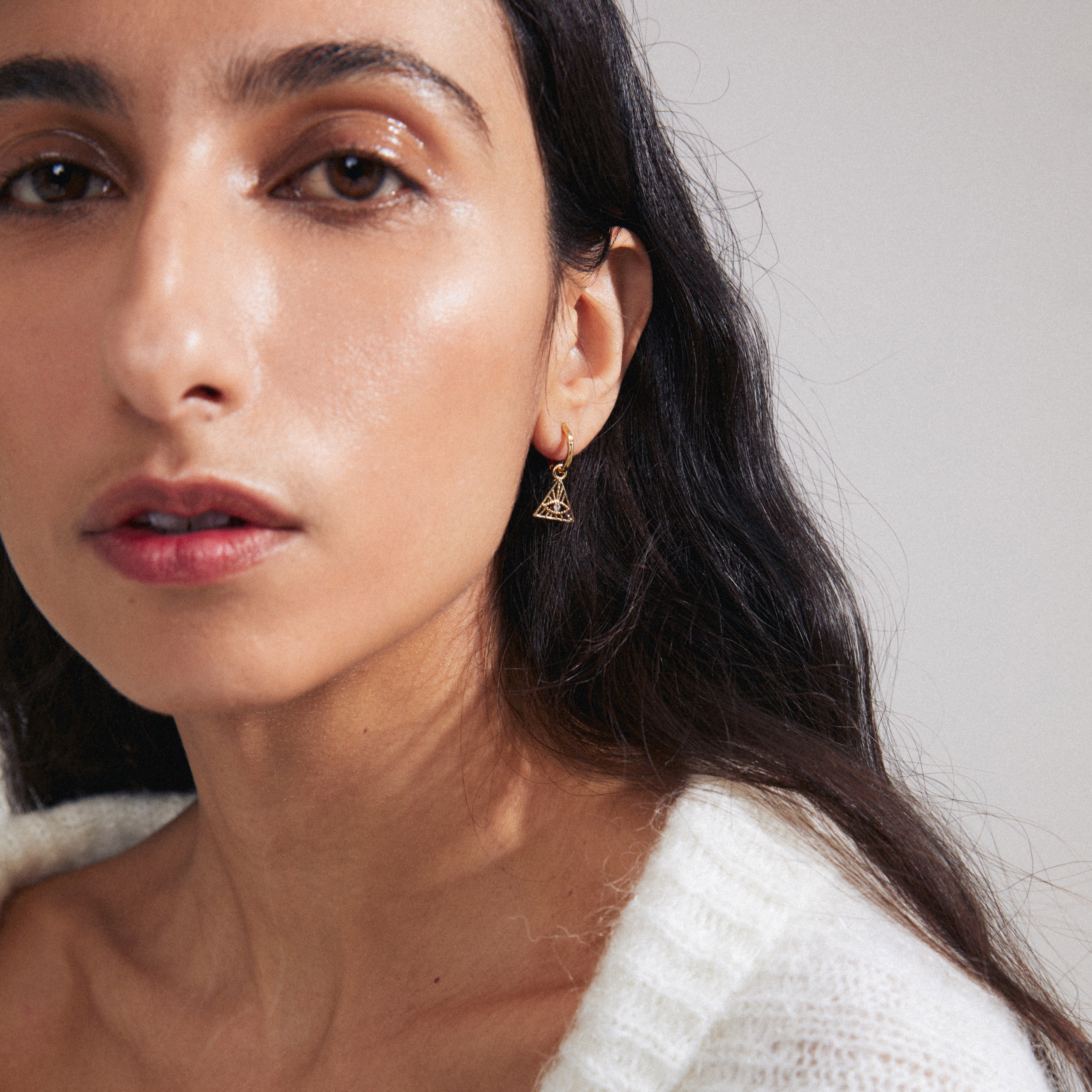 SIBYLLA single earring gold-plated, featuring an all-seeing eye motif with Preciosa crystals, worn by a woman with long hair.