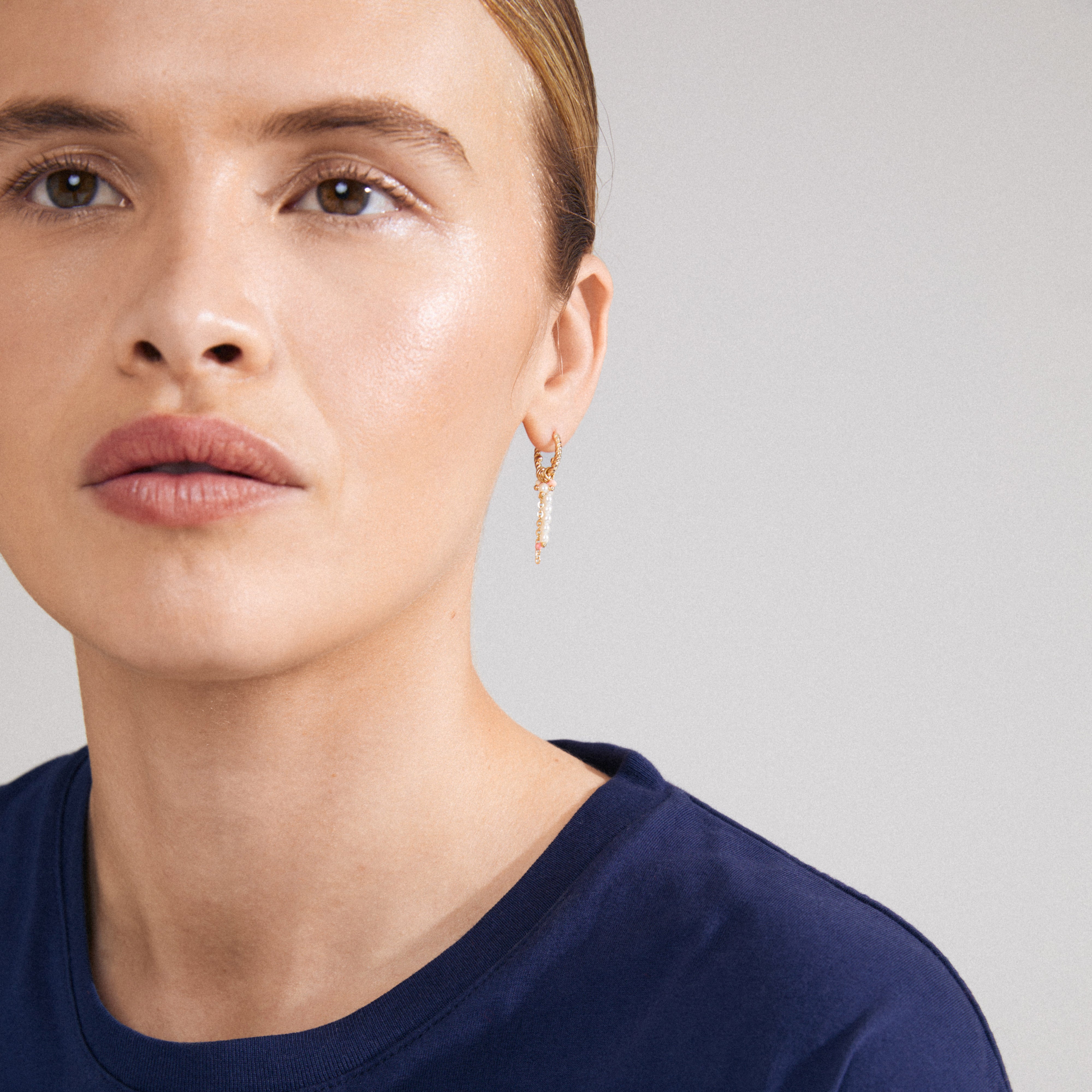 Woman wearing TEKLA single gold-plated earring with romantic pearl pendants, capturing a playful, summery luxe boho vibe. Close-up of face and earring detail.