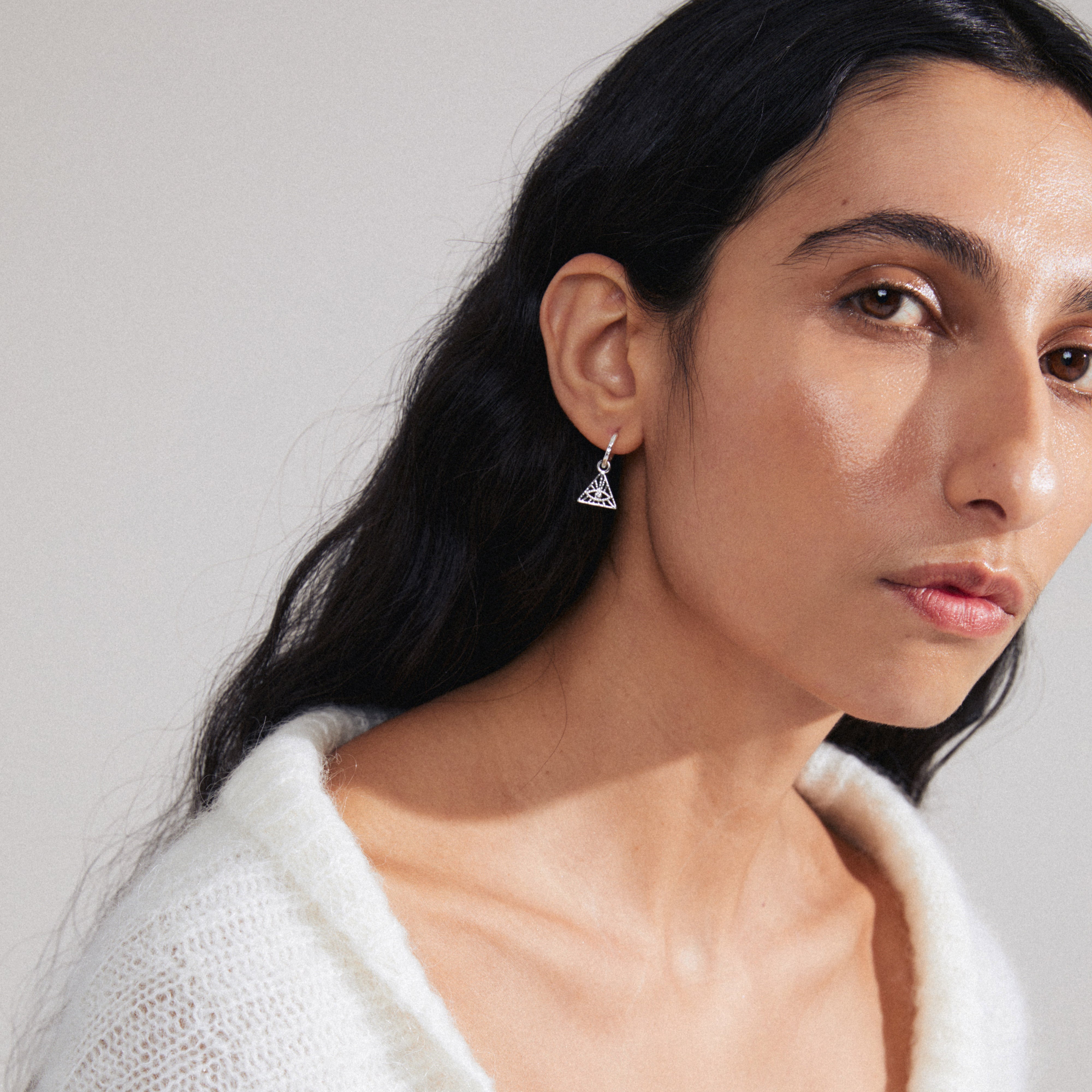 SIBYLLA single earring silver-plated, featuring an all-seeing eye motif within a triangle adorned with Preciosa crystals, worn by a woman with long hair.