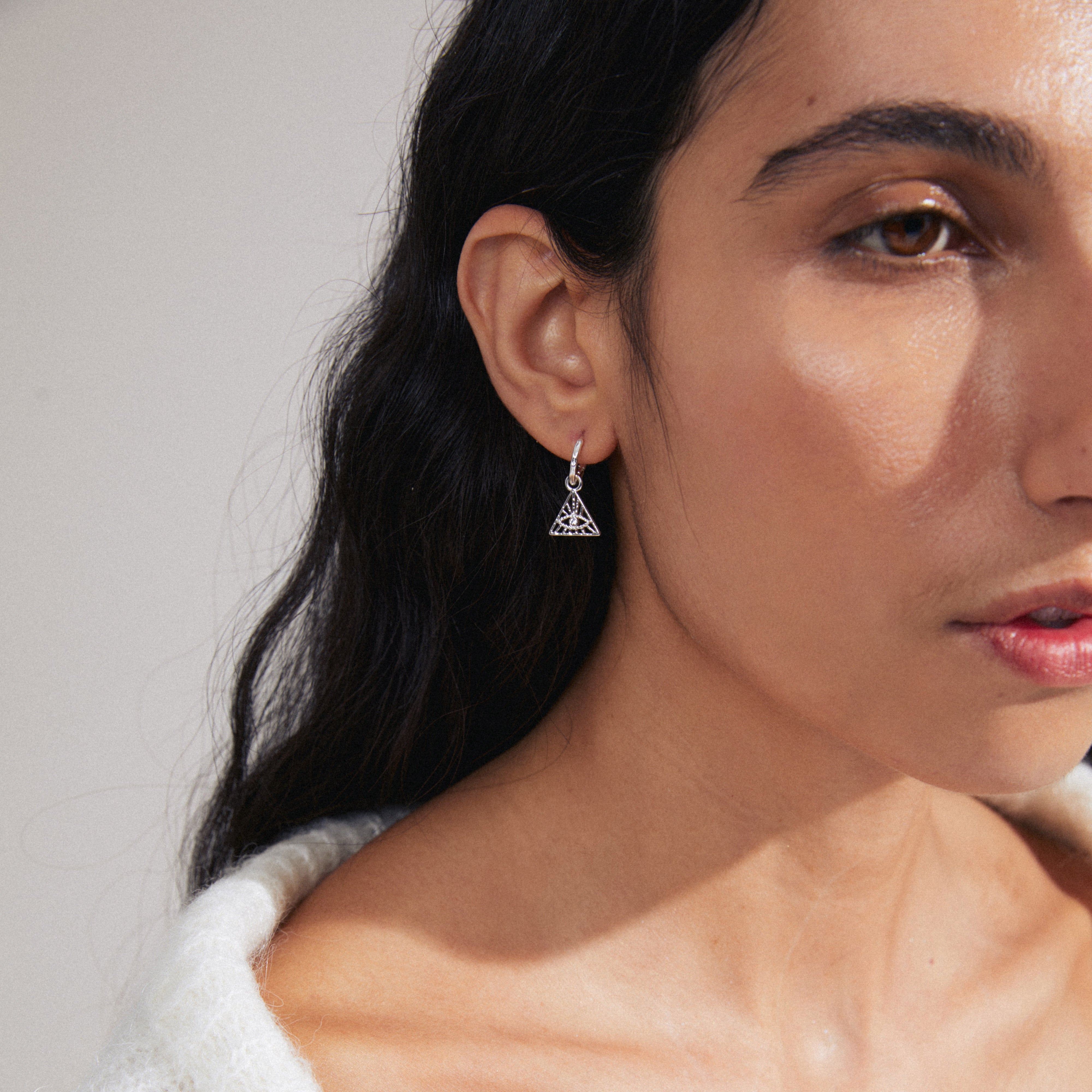 SIBYLLA single earring silver-plated, featuring an all-seeing eye motif with crystals, worn by a woman with long hair and a white sweater.