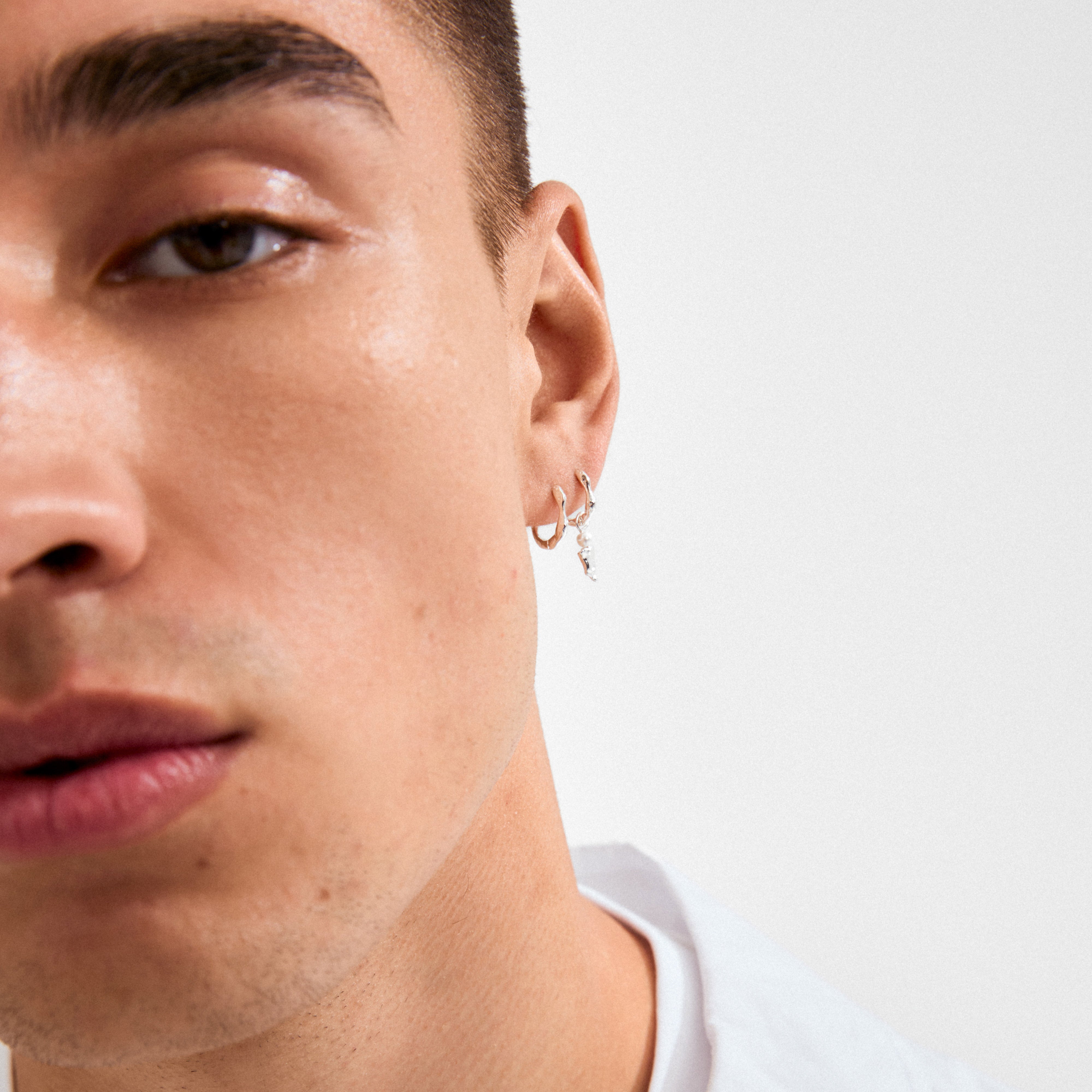 Young man wearing the VASILKI single earring, featuring a silver hoop with a dangling organic-shaped charm and glass bead, styled for a trendy asymmetrical look.