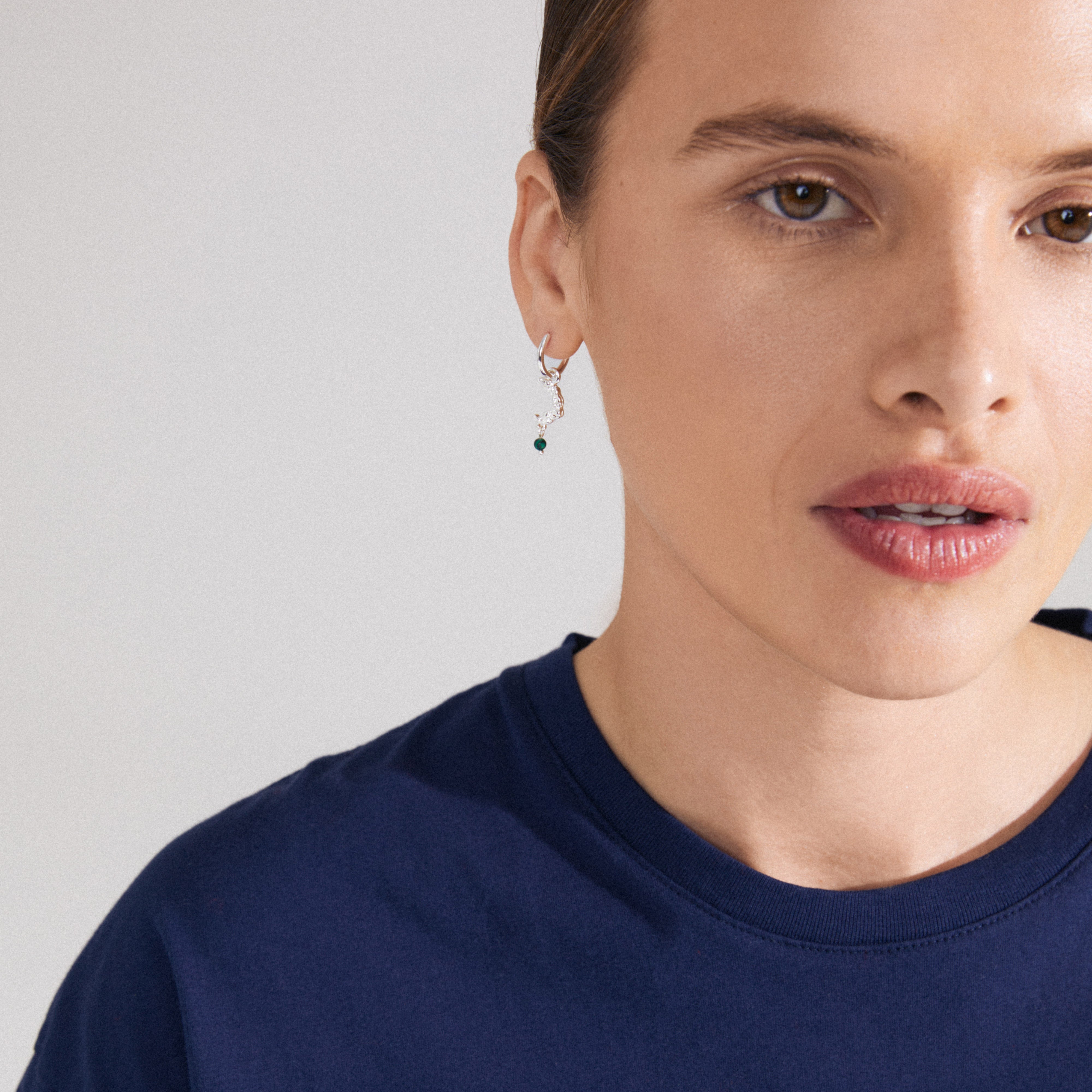 THERA single earring in silver-plated design, featuring a moon pendant with a green stone, worn by a woman in a close-up portrait.
