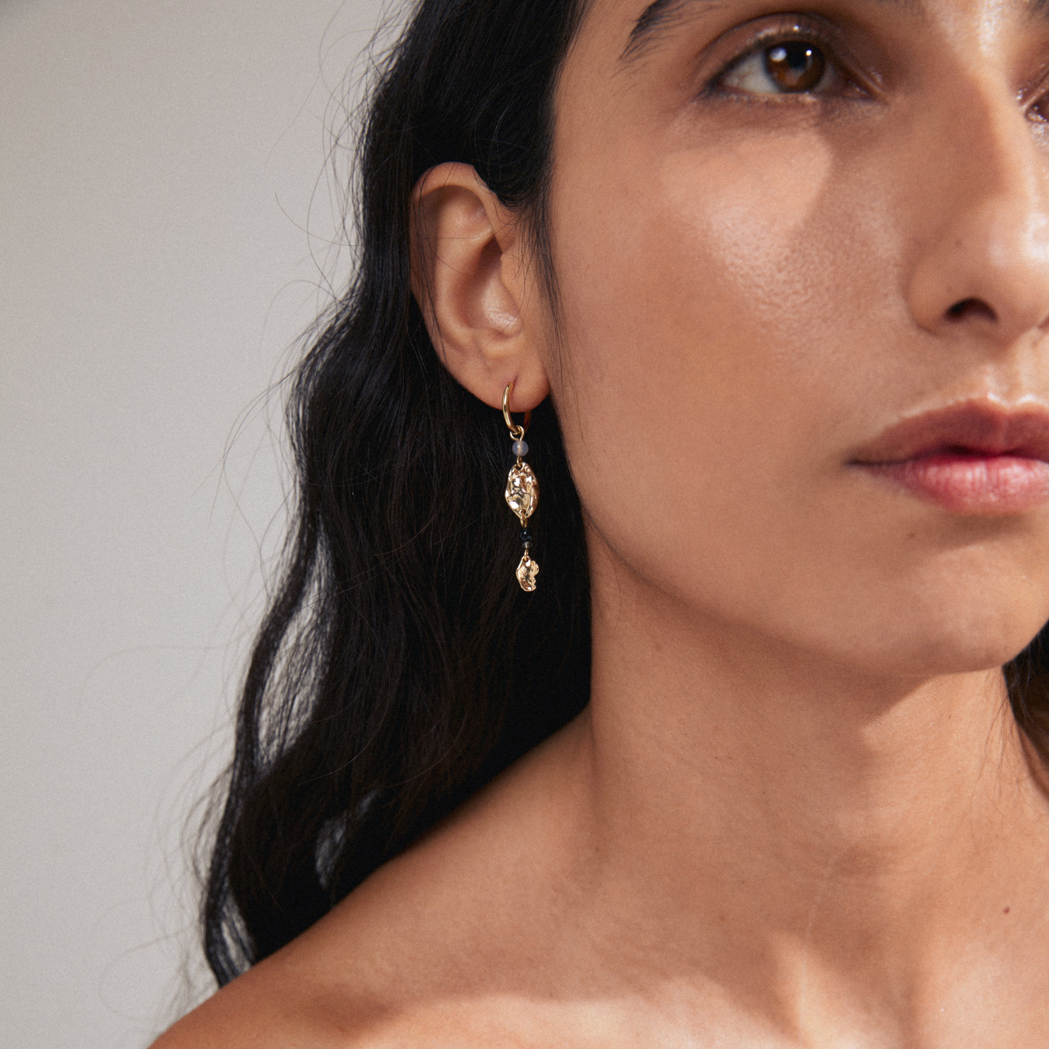 SARRA single earring gold-plated with a gold pendant and black agate bead, worn by a woman with long hair, emphasizing Scandinavian style.