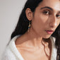 SELENE single gold-plated earring featuring an organic shape with colorful beads, worn by a woman in a white sweater, showcasing a handcrafted, boho style.