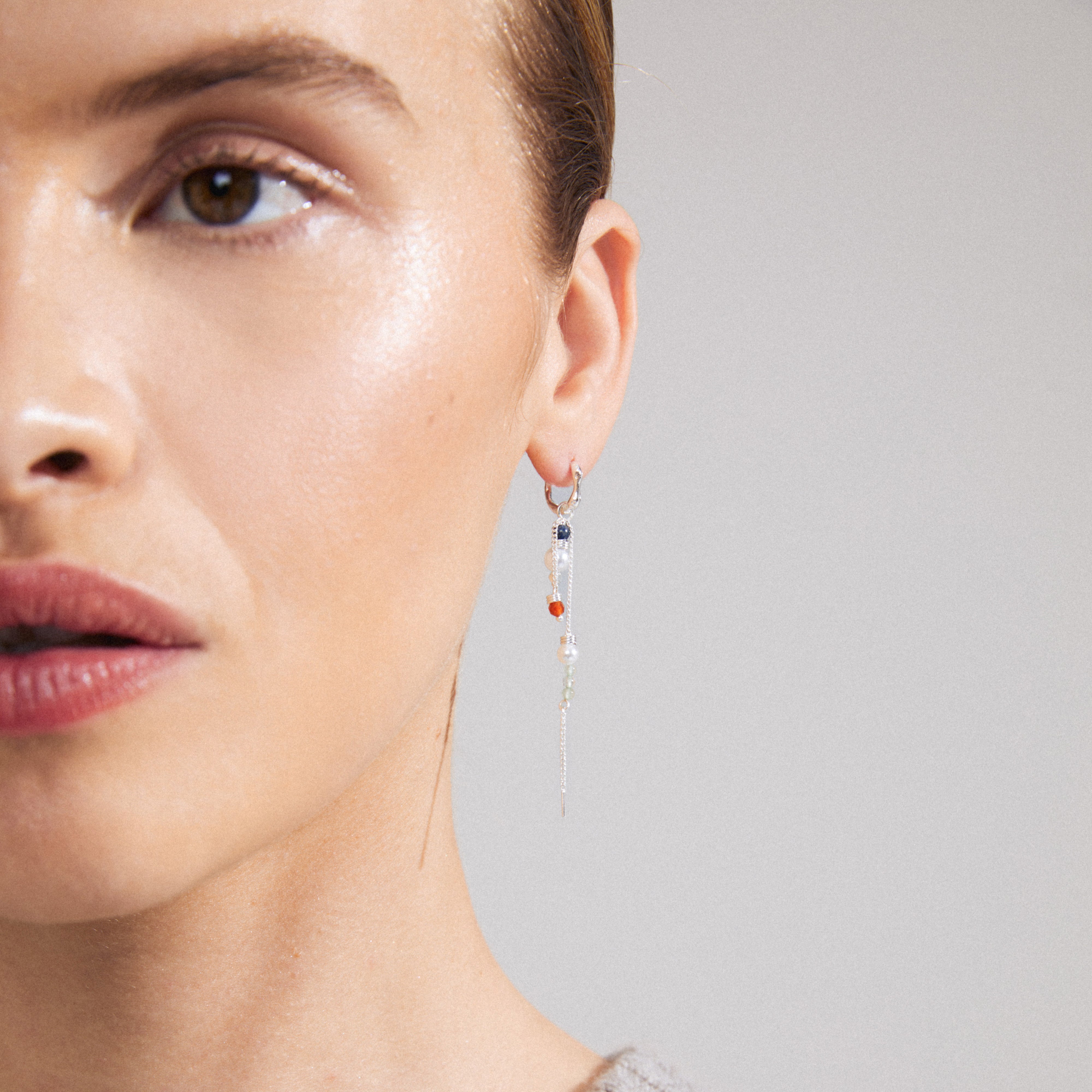 SIBYL single earring, silver-plated hoop with a slender chain and colorful glass beads, worn by a woman.