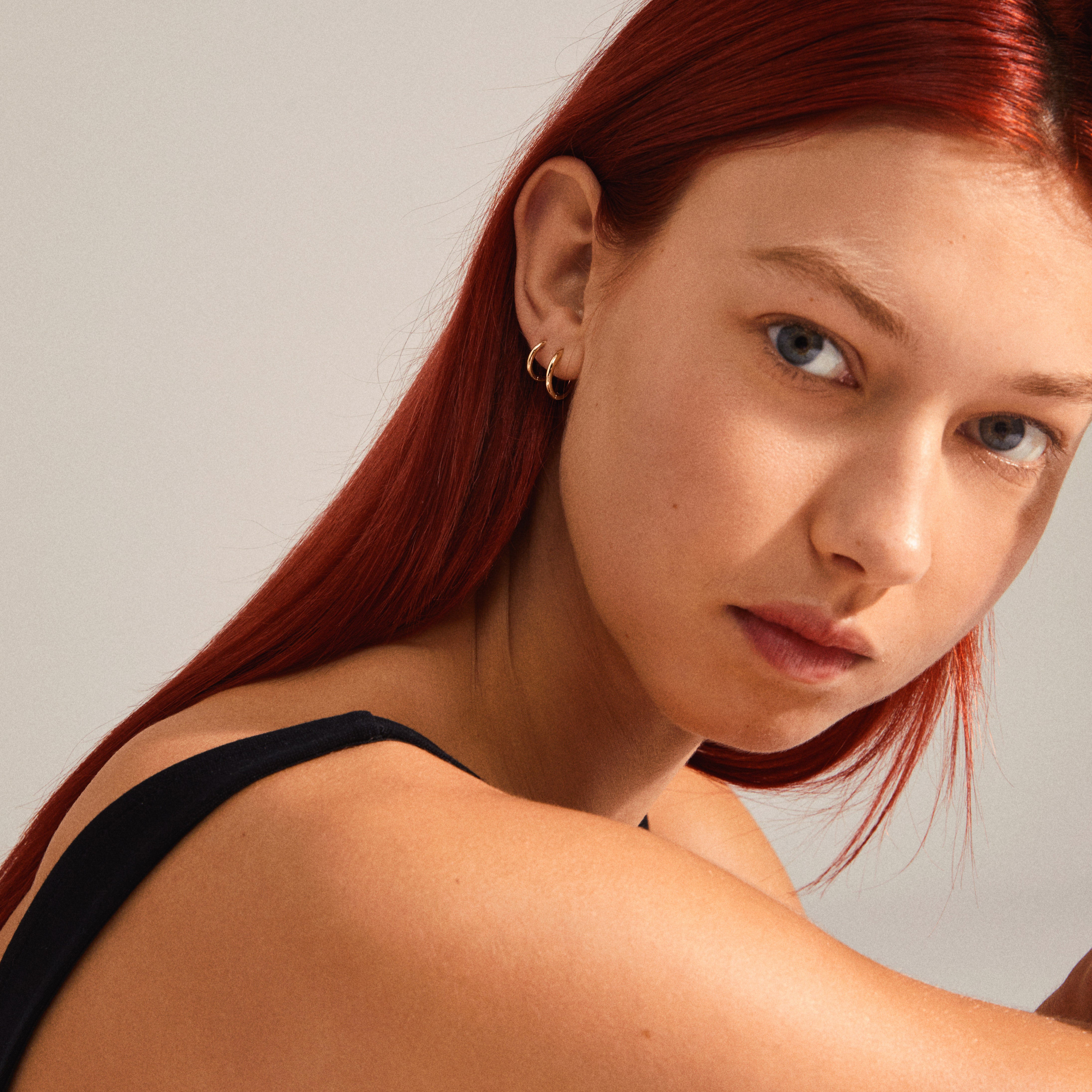LEAF 2-in-1 set huggie hoops gold-plated adorn a red-haired woman, showcasing Pilgrim's timeless, stylish design in a close-up of her ear.