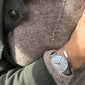 Close-up of a person wearing a gold-plated CHARM F pendant on a chain, alongside a watch, showcasing personalized, stylish jewelry from Pilgrim.