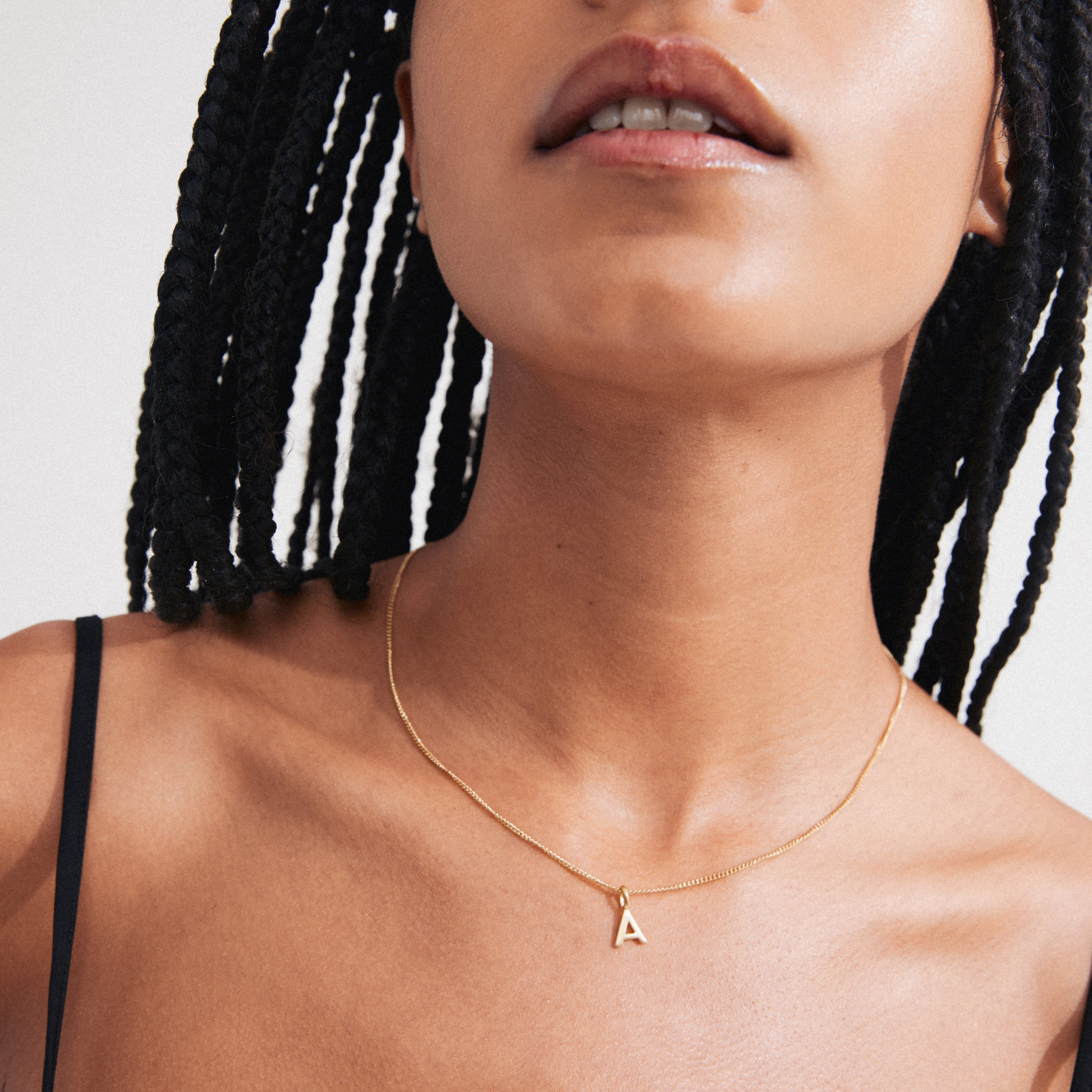 Person wearing CHARM necklace with A pendant, gold-plated, on a delicate chain. The necklace rests on the collarbone, complementing the spaghetti-strap top.