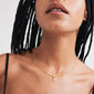 Person wearing CHARM necklace with A pendant, gold-plated, on a delicate chain. The necklace rests on the collarbone, complementing the spaghetti-strap top.