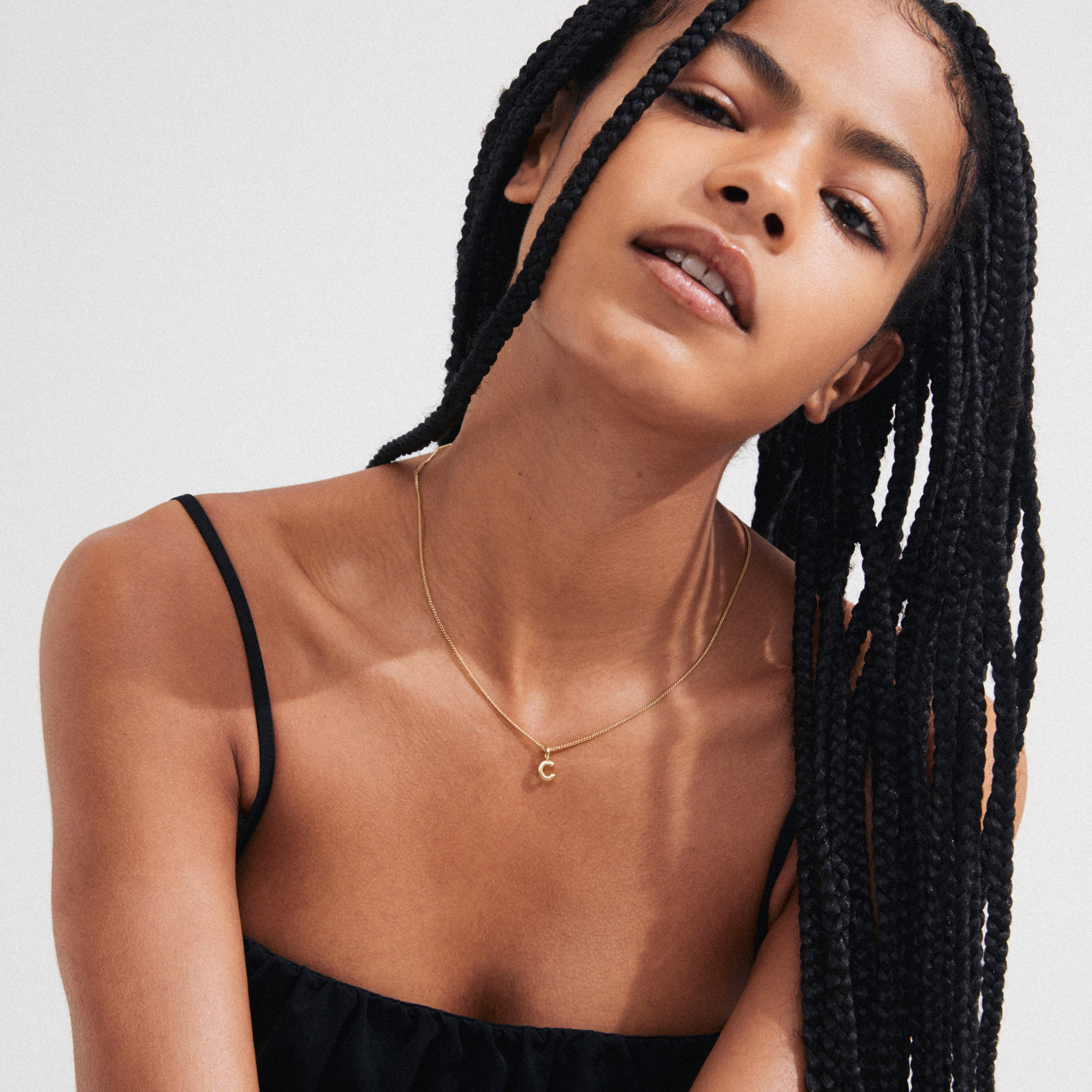 Young woman wearing a CHARM necklace with a gold-plated C pendant, showcasing her personalized style with Pilgrim's elegant, recycled materials.