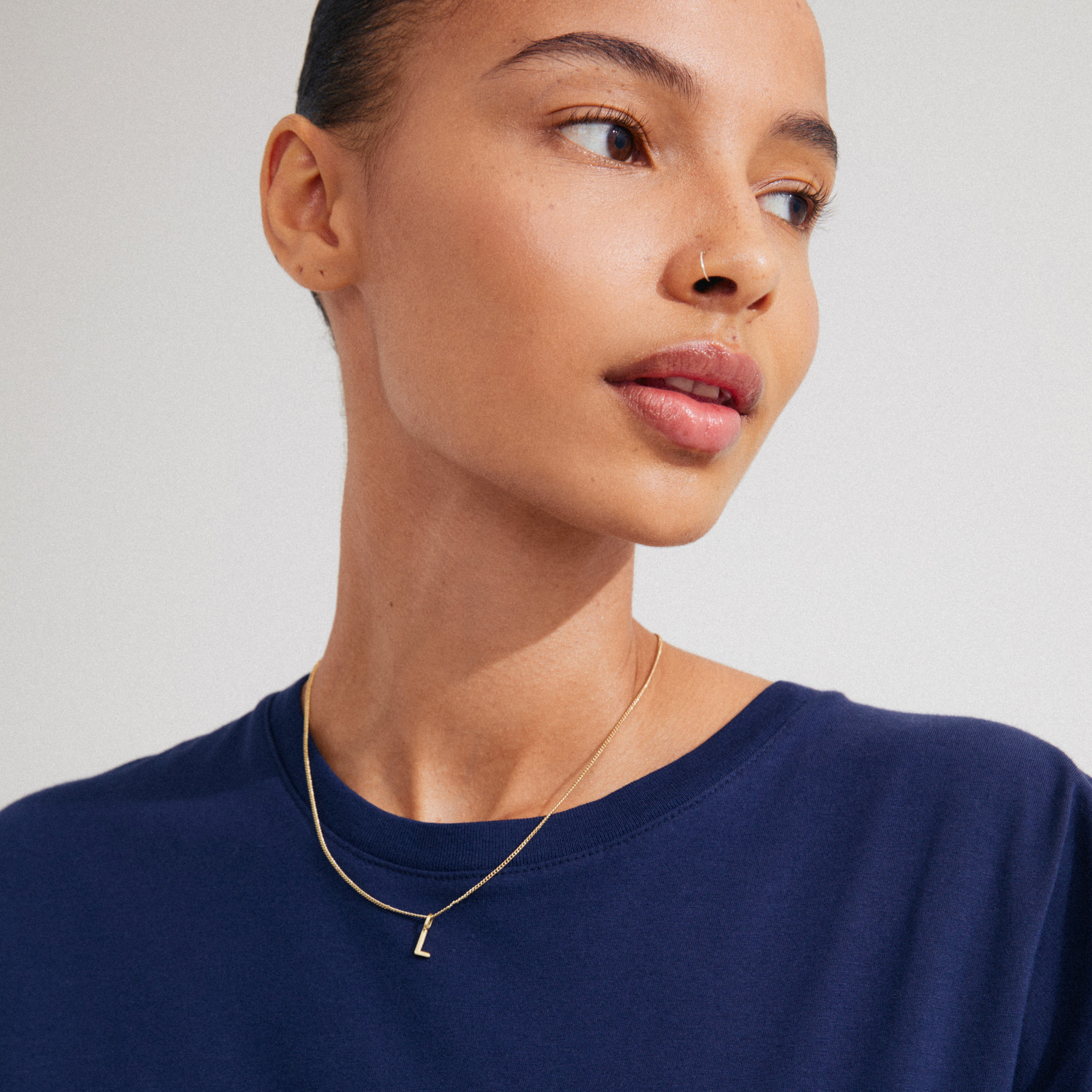 Young woman wearing the CHARM necklace with L pendant, gold-plated, highlighting personalization with a delicate design perfect for adding a bespoke touch to your jewellery collection.