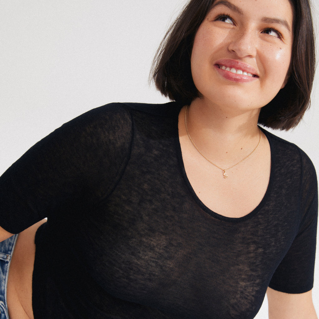 Young woman wearing a CHARM necklace with gold-plated S pendant and semi-sheer black T-shirt, epitomizing Pilgrim's blend of timeless style and personalization.