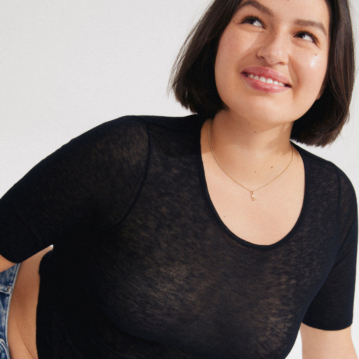Young woman wearing a CHARM necklace with gold-plated S pendant and semi-sheer black T-shirt, epitomizing Pilgrim's blend of timeless style and personalization.
