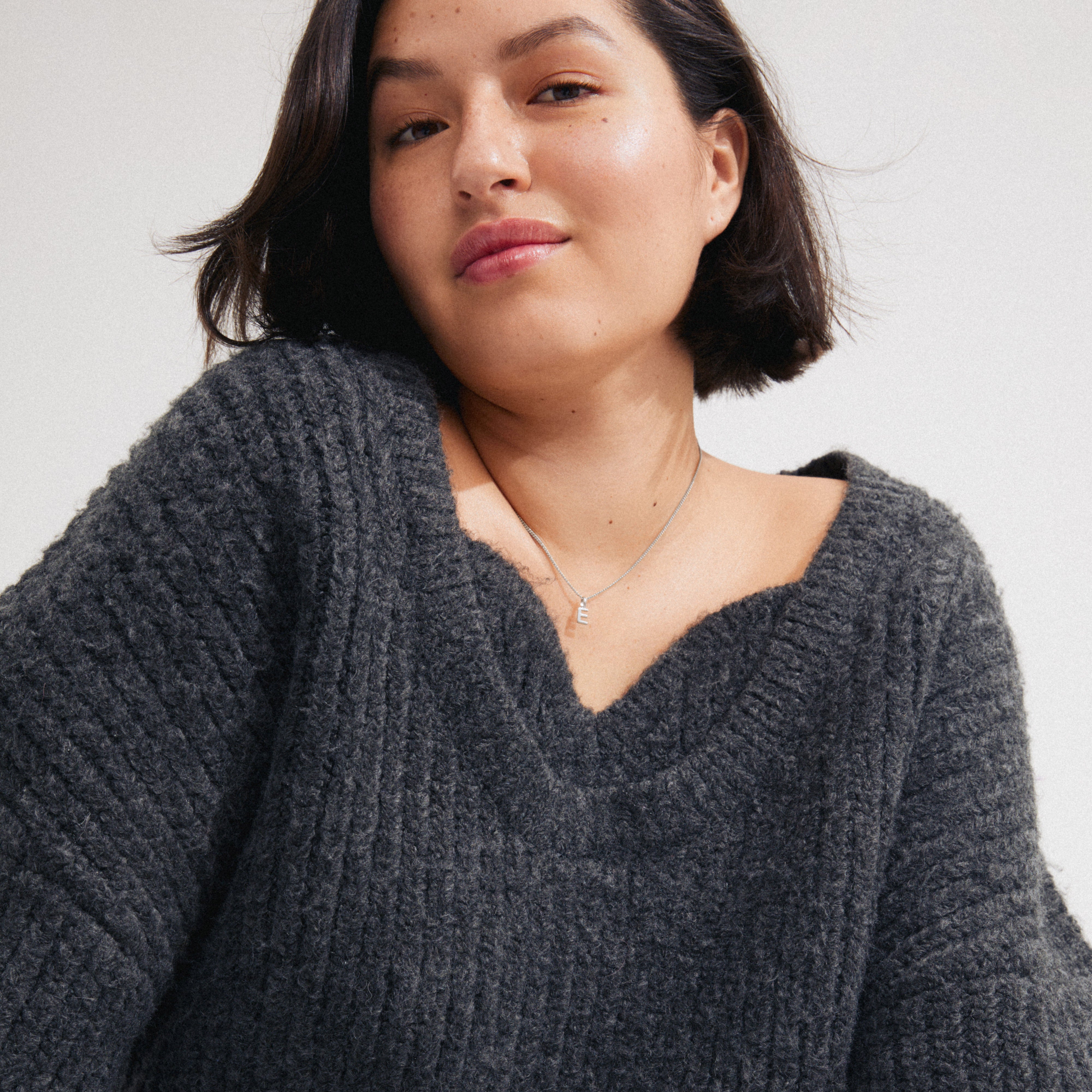 Close-up of a person wearing a chunky sweater and the CHARM necklace with E pendant, silver-plated, highlighting its delicate, personalizable design.