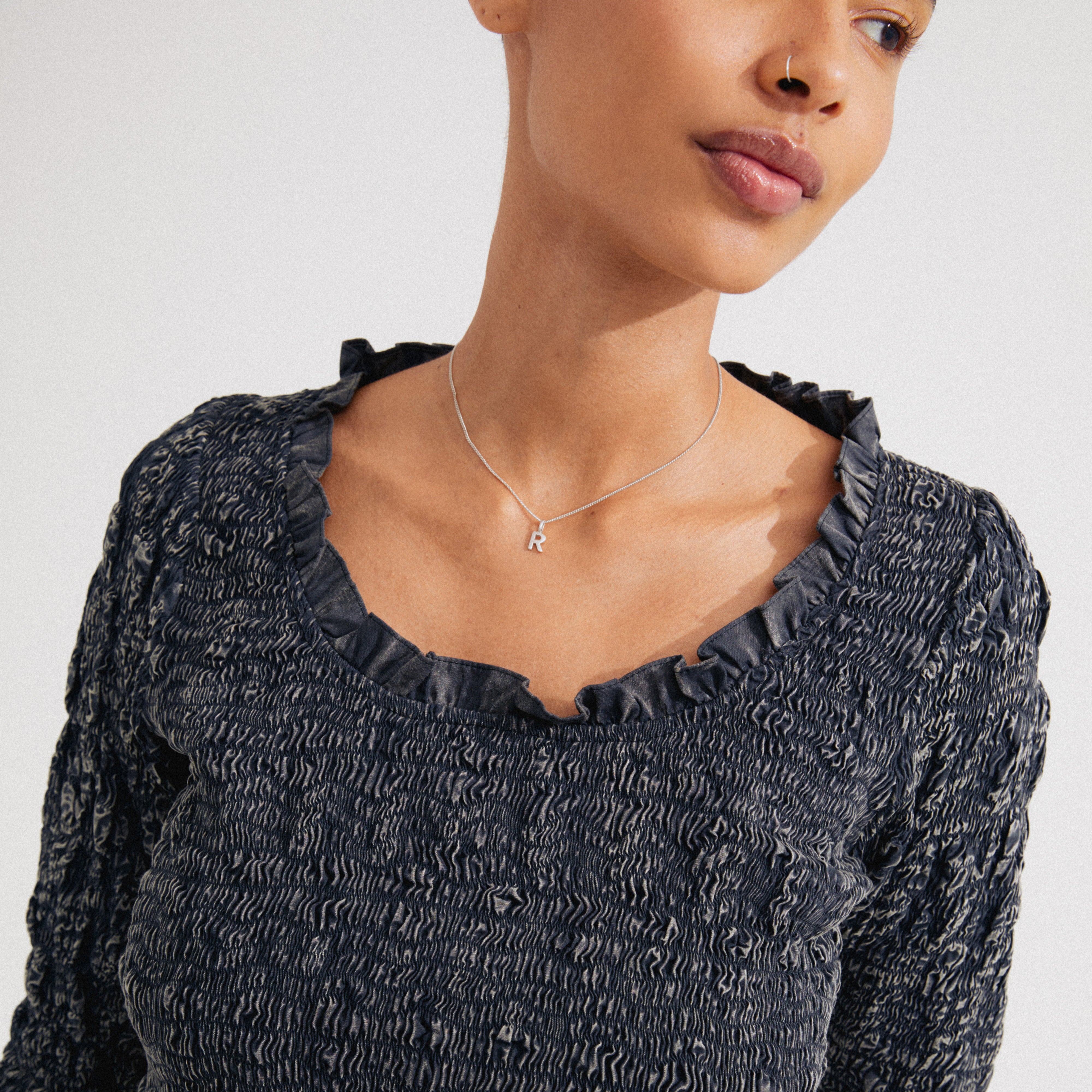 Close-up of a person wearing a CHARM necklace with an R pendant, silver-plated, showcasing personalized style with a fine chain, aligning with Pilgrim’s trendy, inclusive ethos.