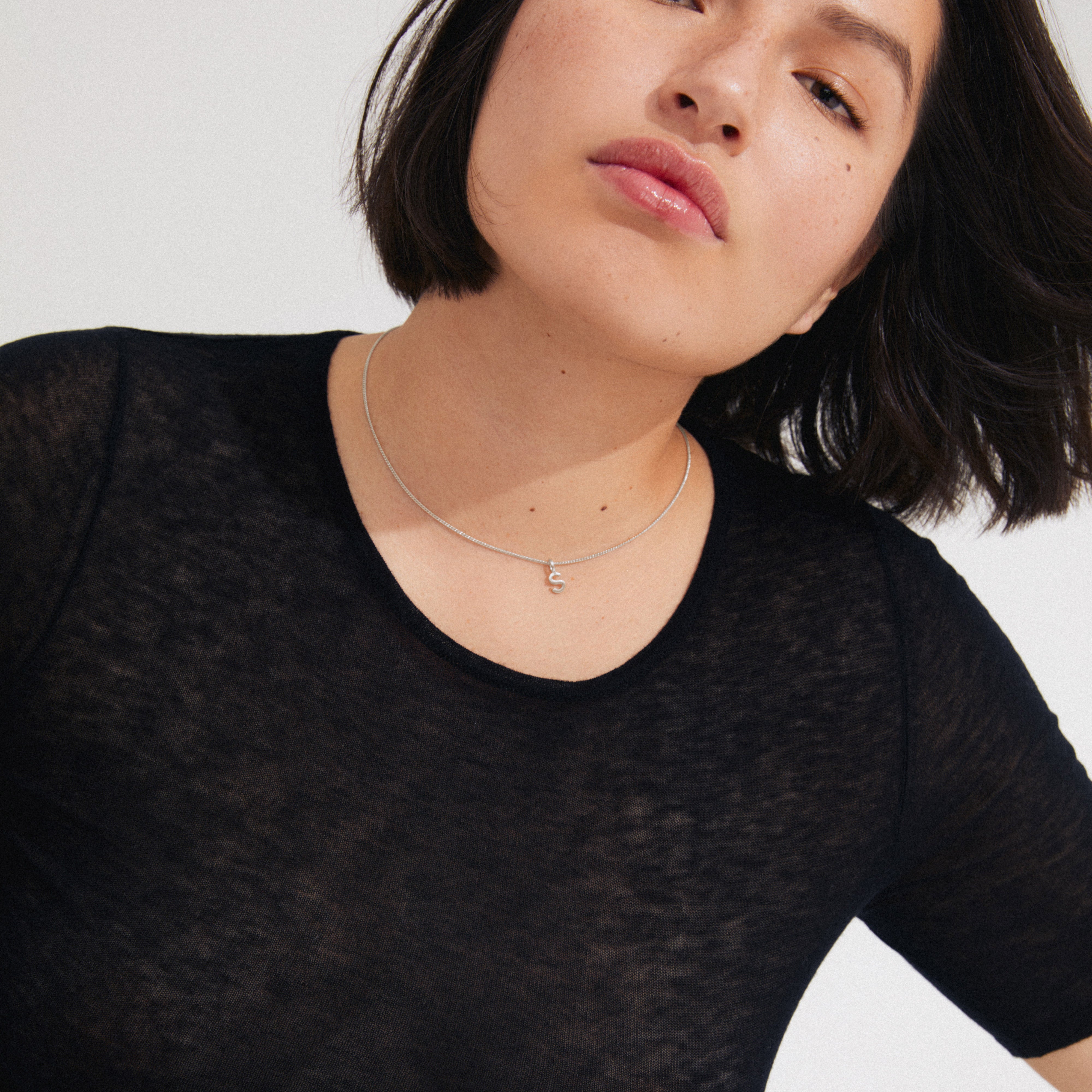 Young woman wearing a CHARM necklace with an S pendant, silver-plated, showcasing a delicate, personalized touch. Perfect for adding bespoke style to your jewelry collection.