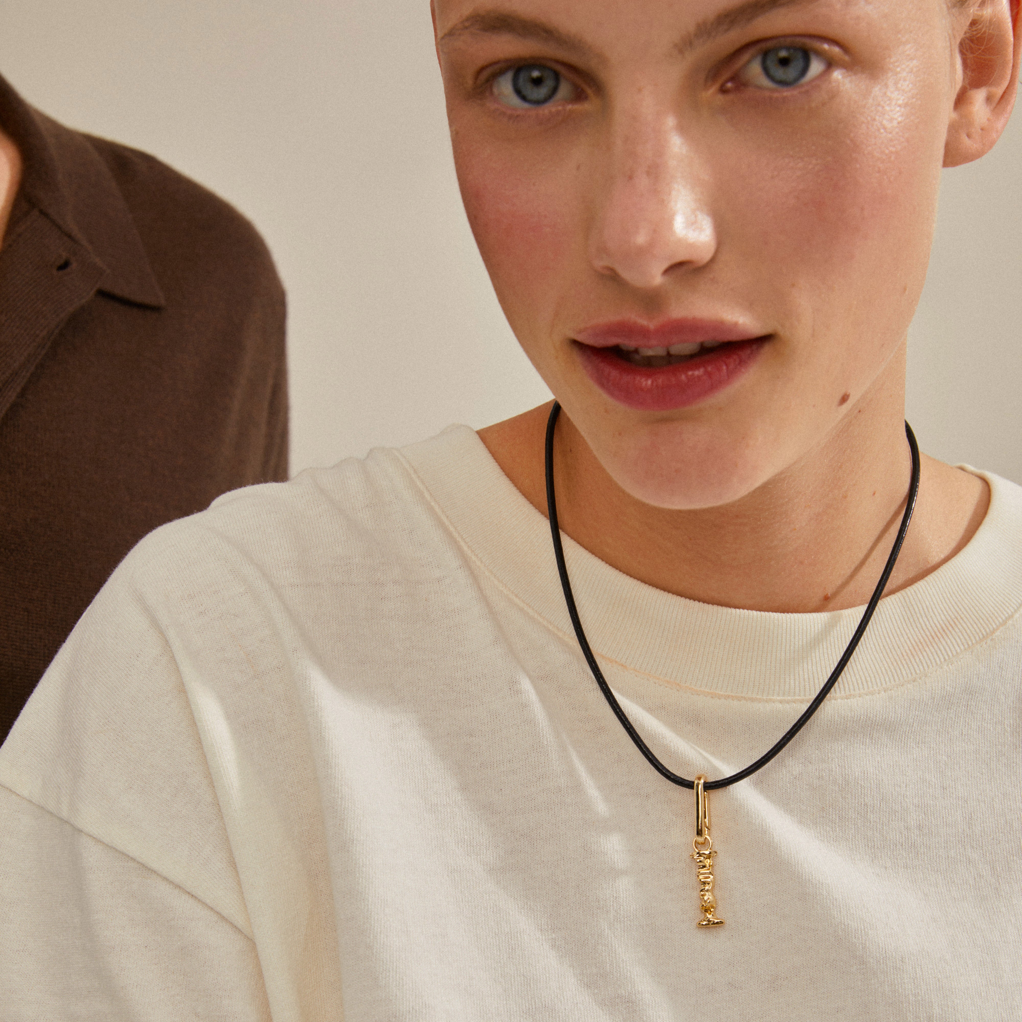 Woman wearing a black necklace showcasing the CHARM pendant I, gold-plated, from Pilgrim, highlighting its personalized and stylish design.