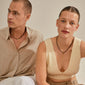 A man and woman showcase Pilgrim's CHARM pendant J, gold-plated, styled with necklaces, highlighting personal and unique fashion expressions.