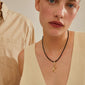 A woman wears the CHARM pendant K, gold-plated, showcasing Pilgrim's artisanal touch with personalized style options, emphasizing sustainable craftsmanship.
