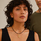 Woman wearing a black dress and necklace, showcasing Pilgrim's gold-plated CHARM pendant N, designed for personalized style with recycled materials.