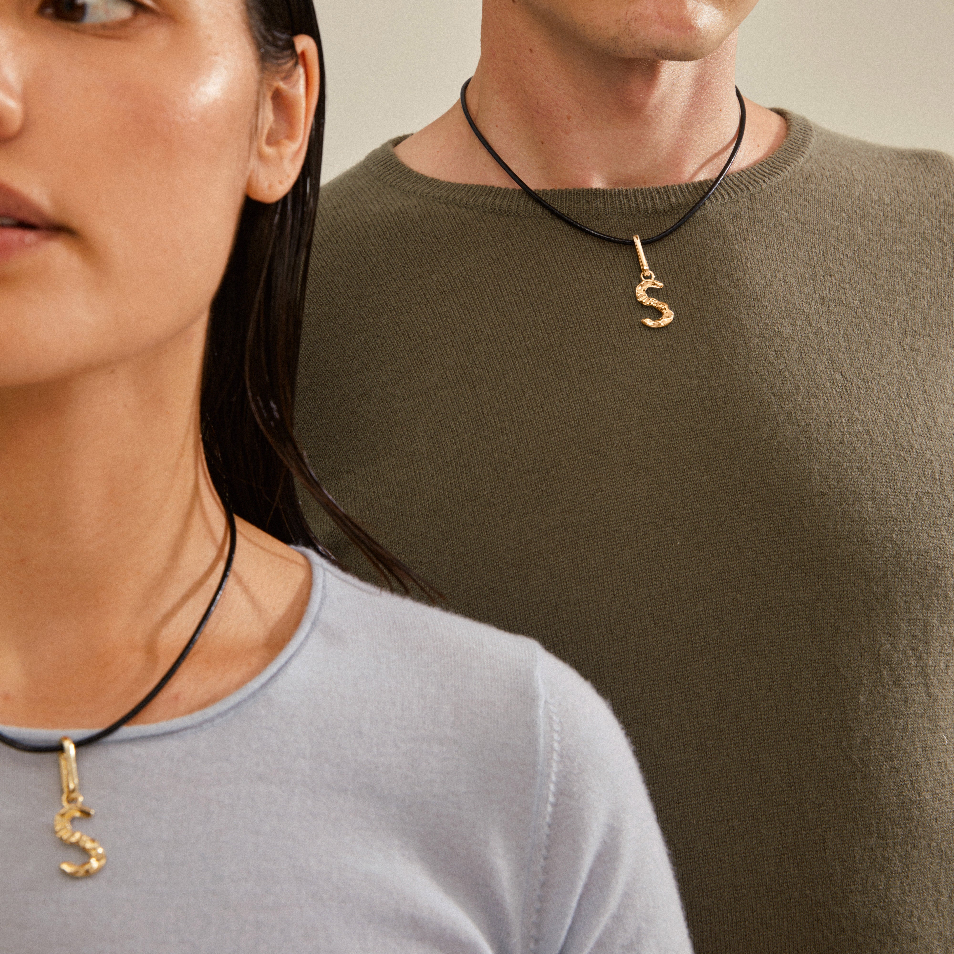 A man and woman showcasing Pilgrim's CHARM pendant S, gold-plated, worn on necklaces, highlighting its personalized and sustainable design.