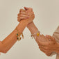 Two hands clasping, showcasing the CHARM curb chain bracelet gold-plated on the left wrist, adorned with dangling charms, highlighting edgy, recycled urban style.