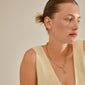 A woman wearing a CHARM coin pendant, gold-plated, showcasing Pilgrim's unique, customizable style with recycled materials.