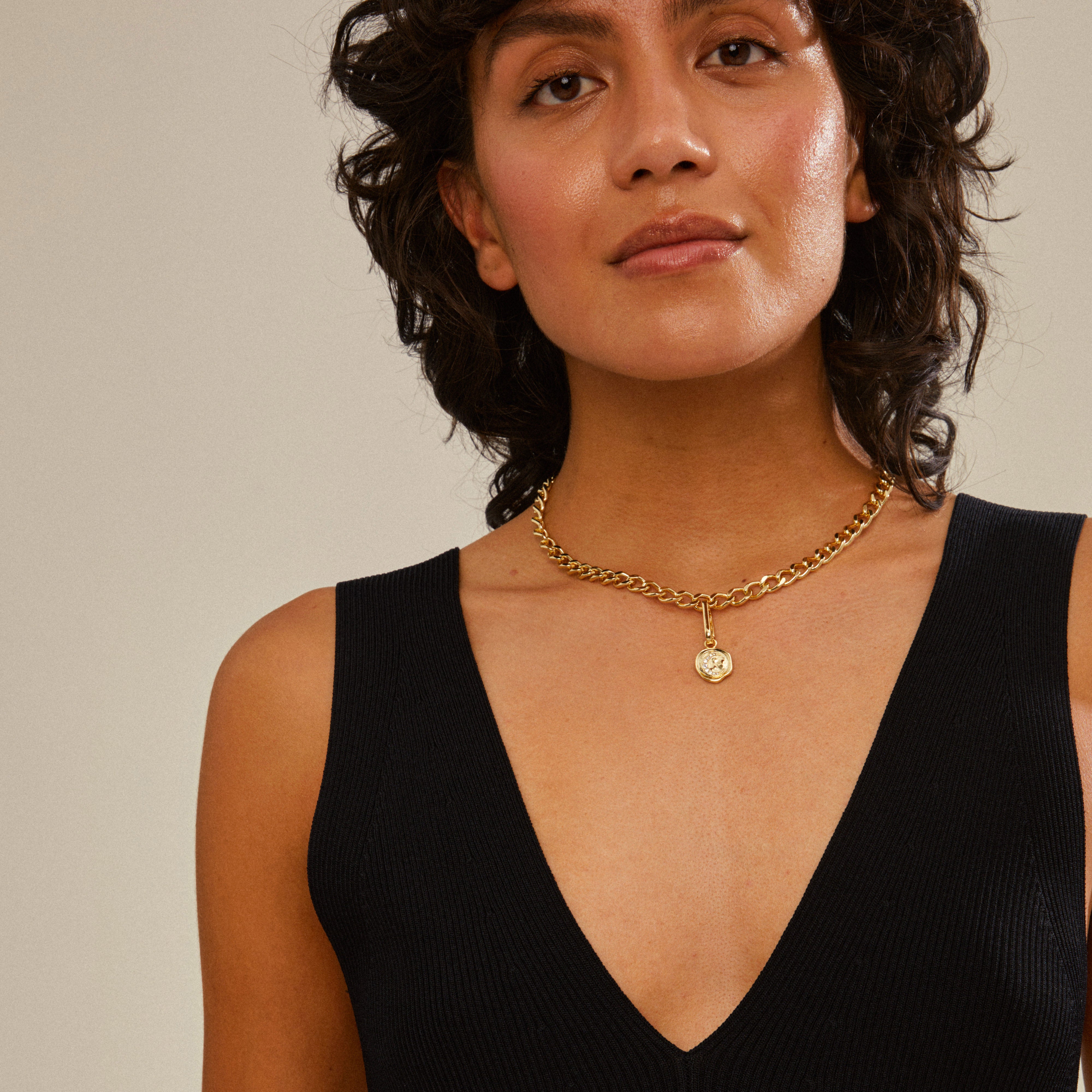 Gold-plated moon pendant on woman wearing a black dress, showcasing Pilgrim's CHARM collection, emphasizing recycled materials and personal style.