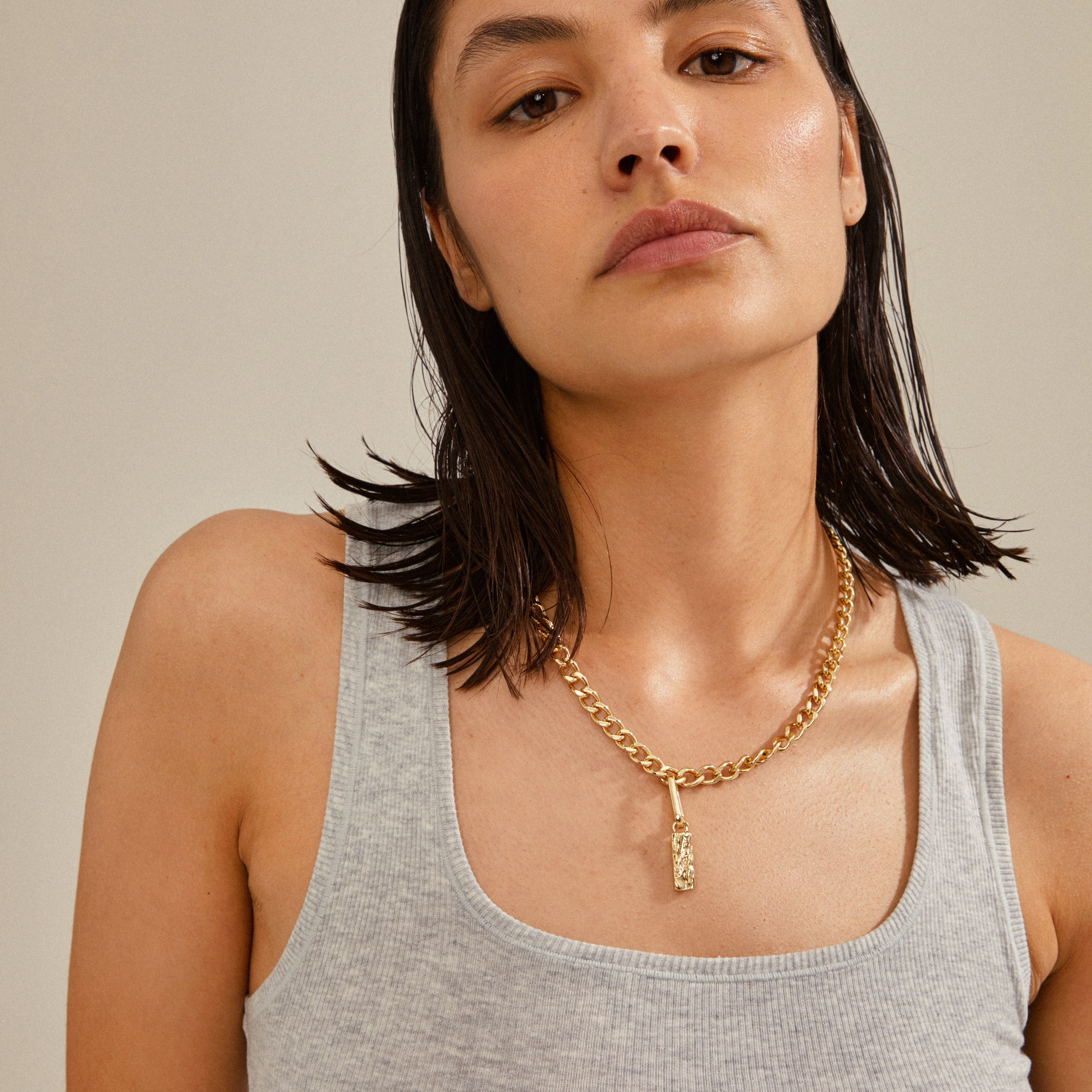 A woman with wet hair wears a gold-plated CHARM tag pendant necklace, showcasing Pilgrim's unique and personalized style.
